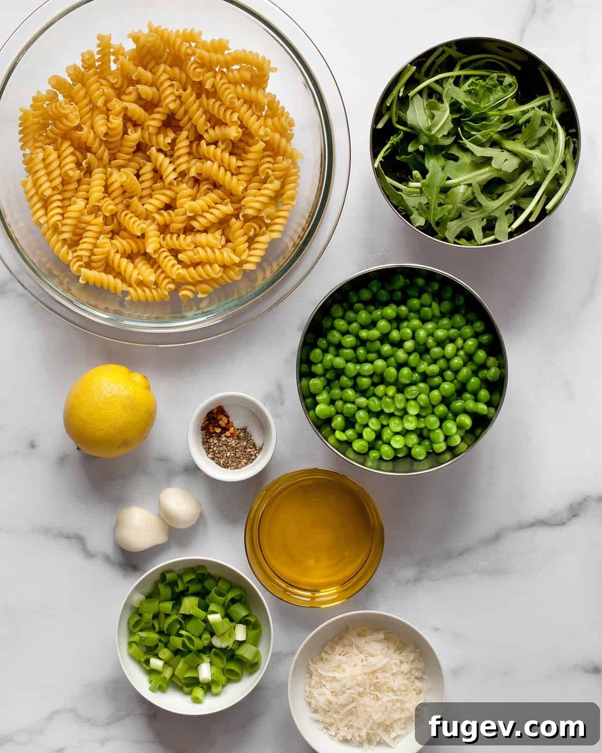 Emerald Green Pea Pesto Pasta 3 A flat lay of fresh ingredients for pea pesto pasta: pasta, thawed frozen peas, lemon, fresh arugula, garlic cloves, olive oil, salt, and pepper.