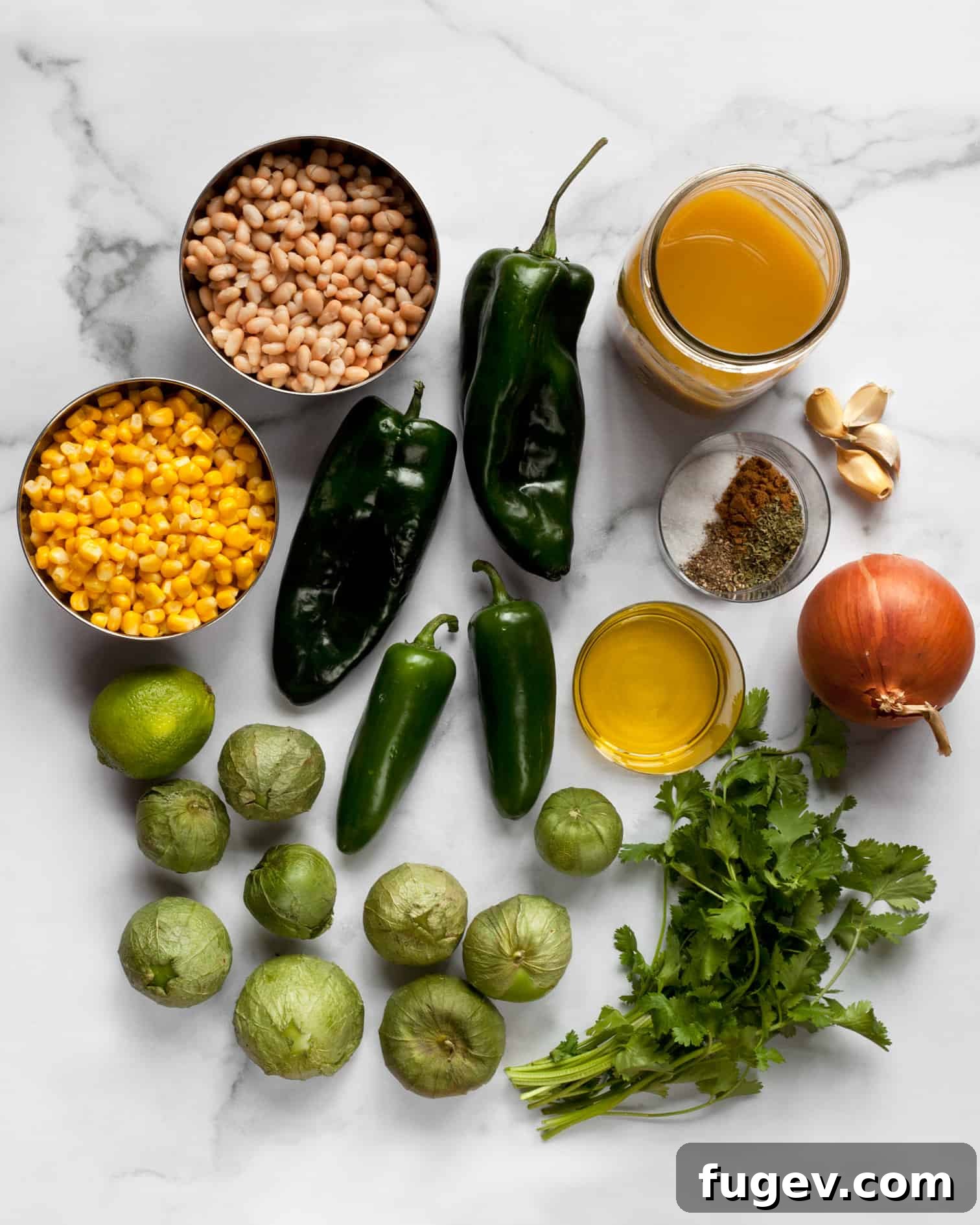 Flavorful Chile Verde with Creamy White Beans 4 Fresh ingredients laid out on a wooden board, including bright green tomatillos, dark green poblano peppers, and vivid green jalapenos.