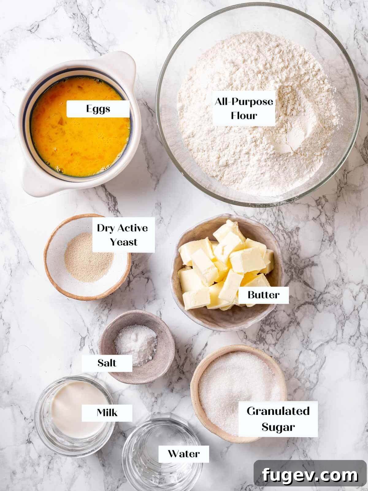 Golden Buttery Brioche Loaf 4 Brioche bread ingredients, including flour, eggs, butter, sugar, and yeast, arranged on a white marble countertop.