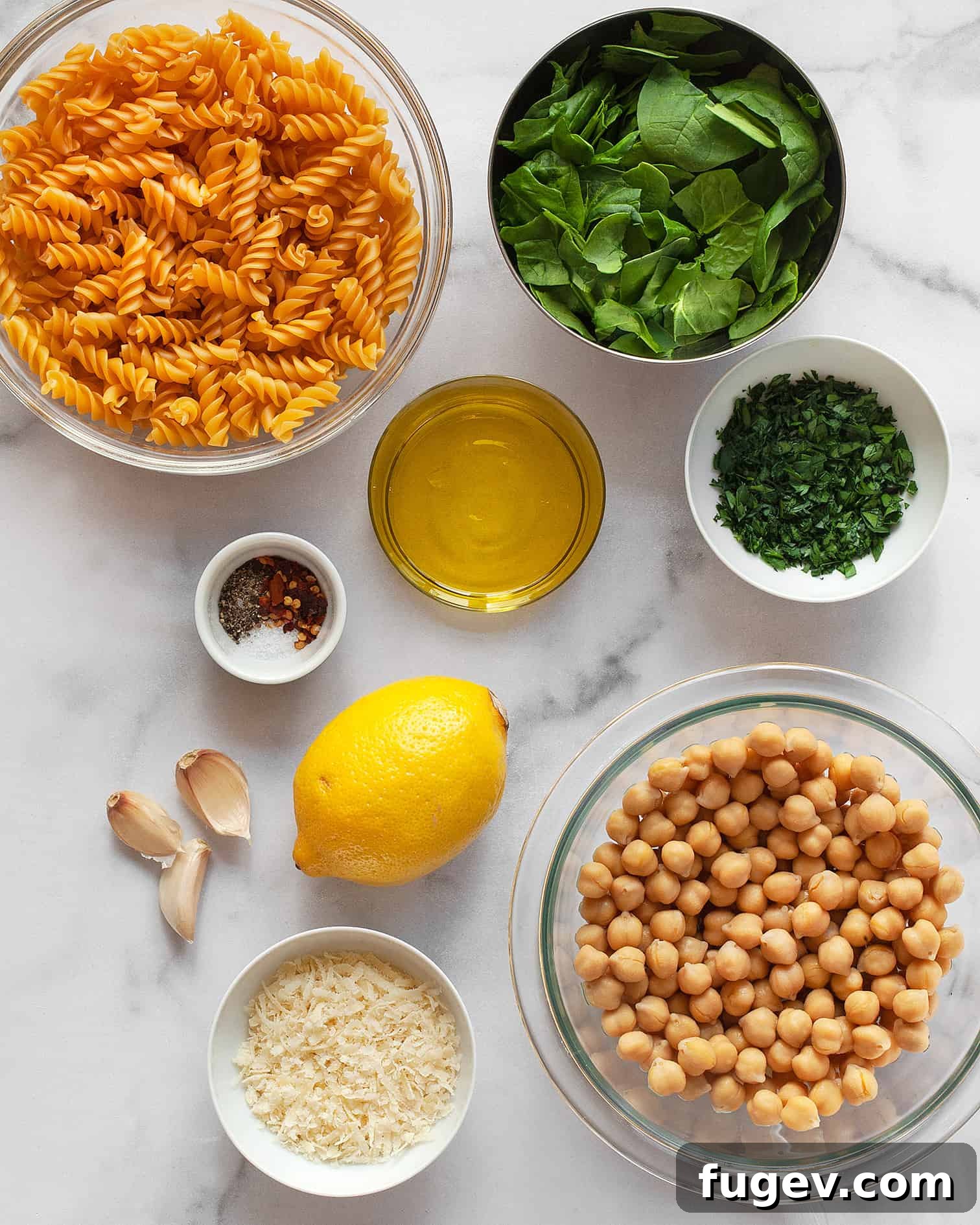 Hearty Spinach Chickpea Pasta 3 A vibrant flat lay photo displaying the key ingredients for chickpea pasta: rotini pasta, fresh lemon, bright spinach, garlic cloves, a can of chickpeas, and a block of Pecorino cheese.