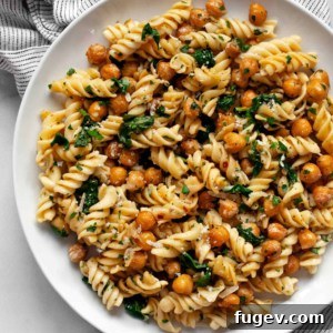 Hearty Spinach Chickpea Pasta 8 Chickpea pasta with spinach on a plate, garnished with fresh herbs and lemon wedges.