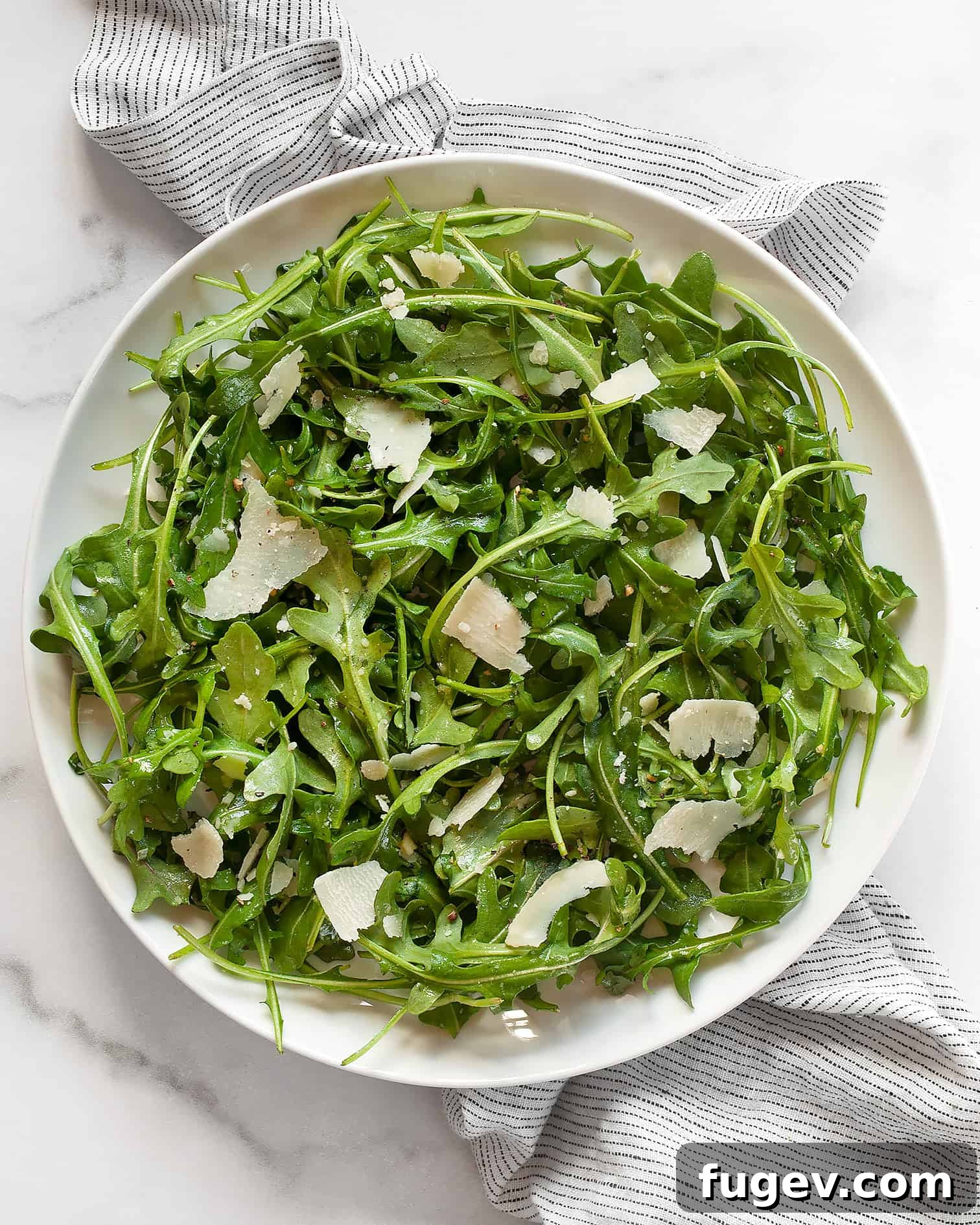 Lemon-Kissed Arugula Salad 2 A vibrant arugula salad with lemon vinaigrette and shaved Parmesan on a white plate, ready to be served.