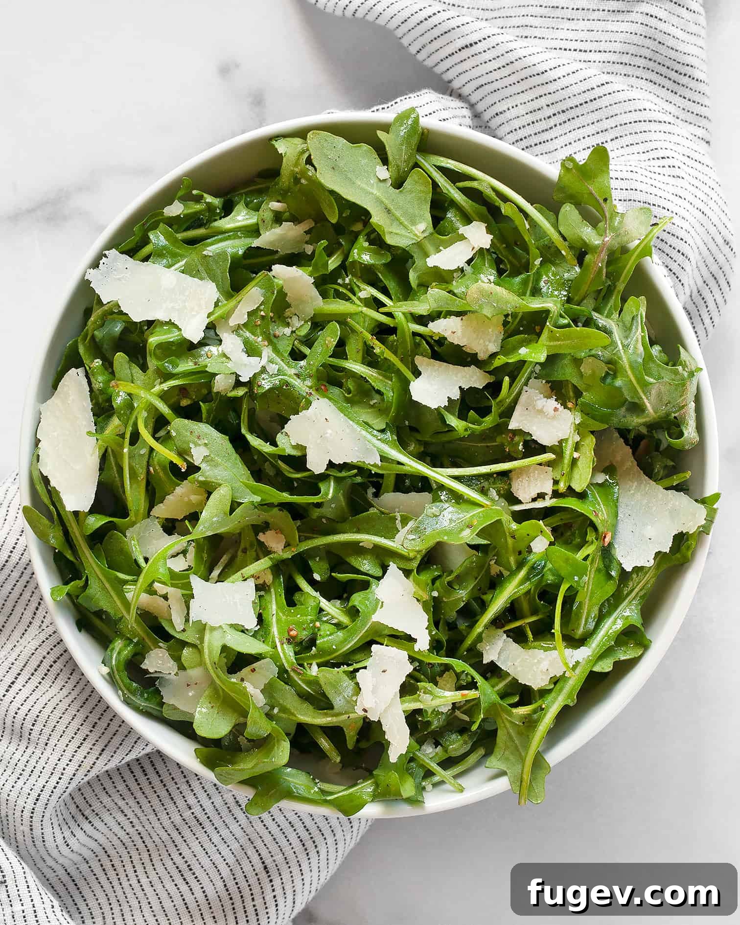 Lemon-Kissed Arugula Salad 5 A close-up shot of the arugula salad with lemon vinaigrette and shaved Parmesan in a rustic white bowl, showcasing its freshness.