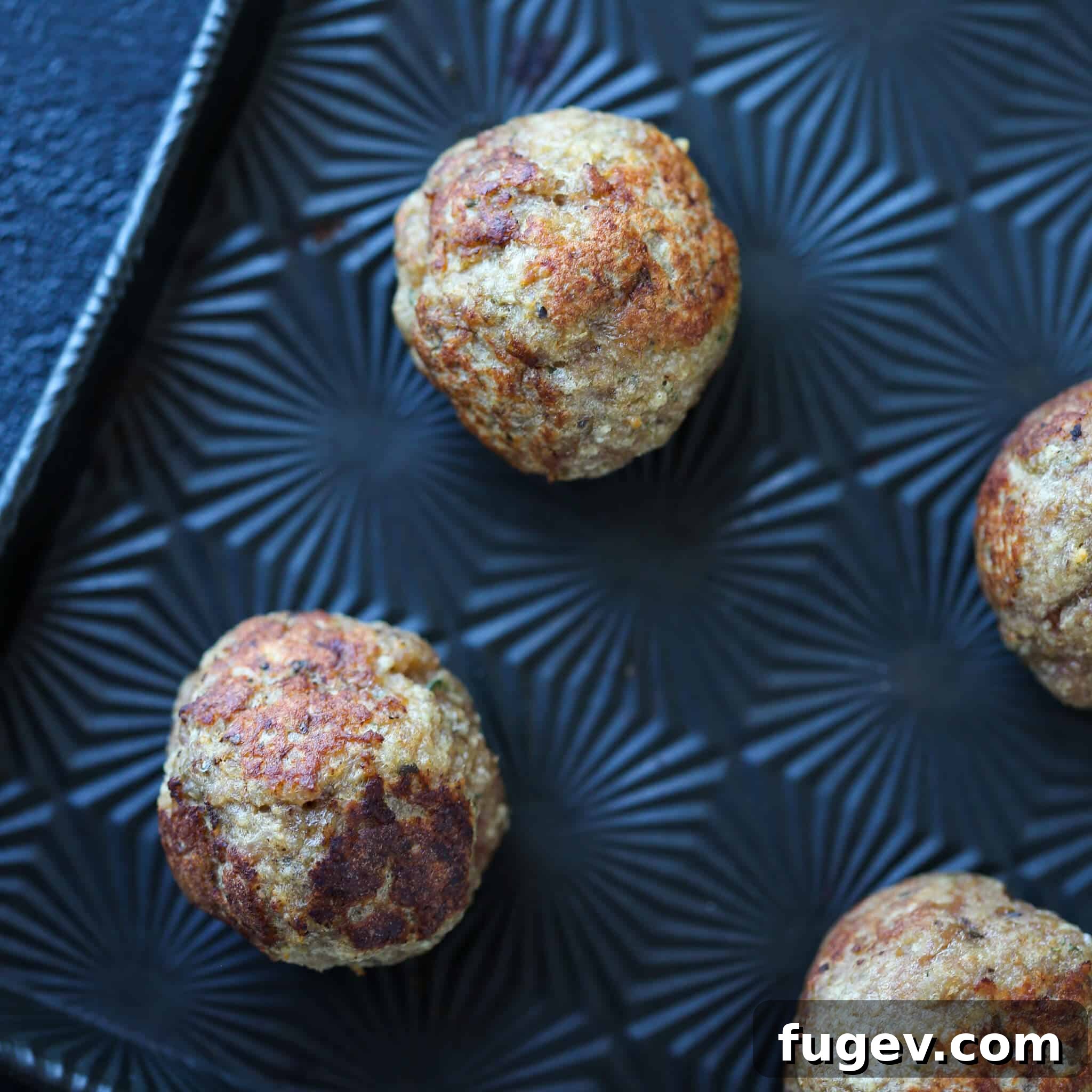 Juicy Baked Turkey Meatballs 3 Baked turkey meatballs browning on a black sheet pan before baking.