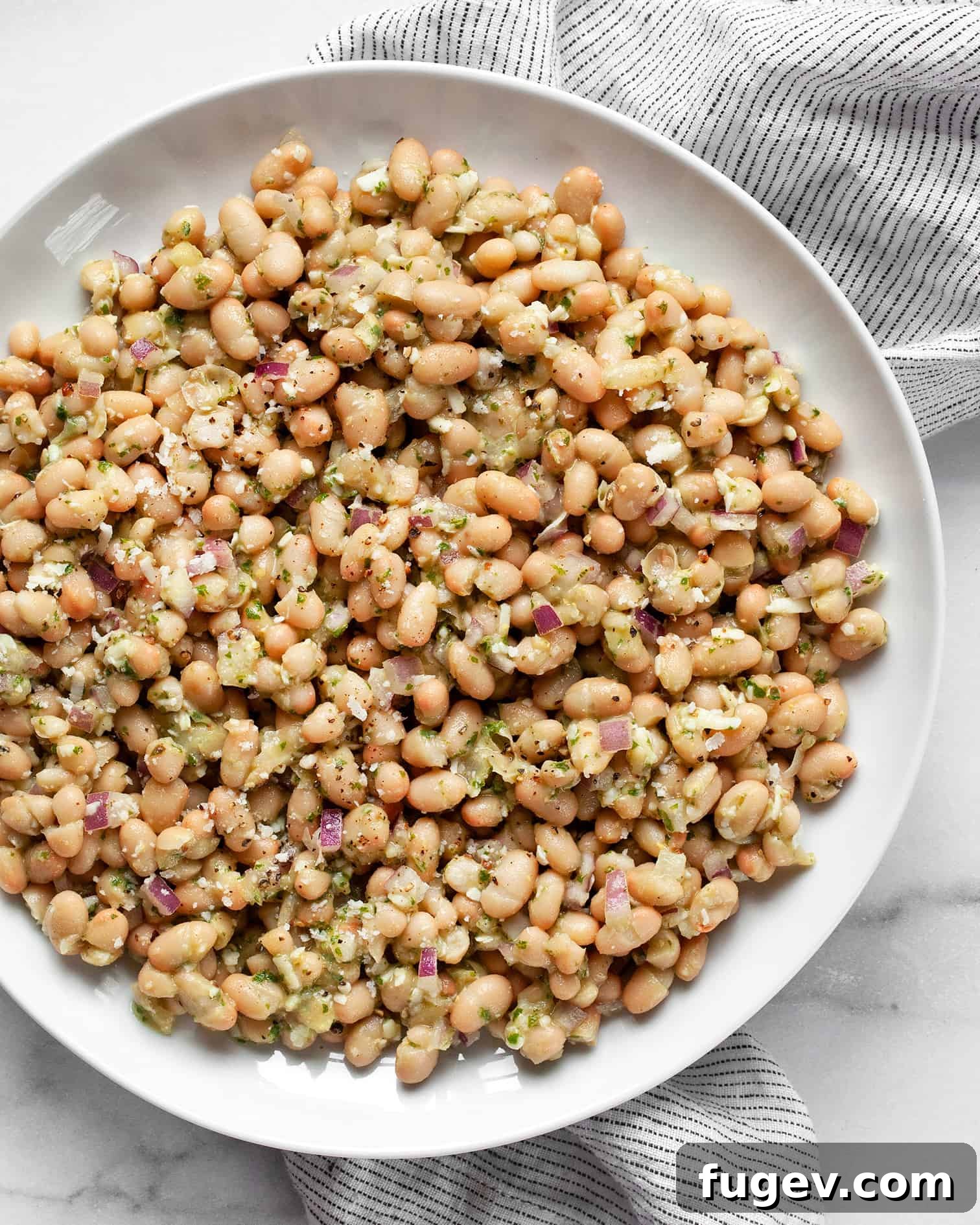Zesty Lemon Basil White Bean Salad 6 A single serving of white bean salad on a white plate, garnished with fresh basil.