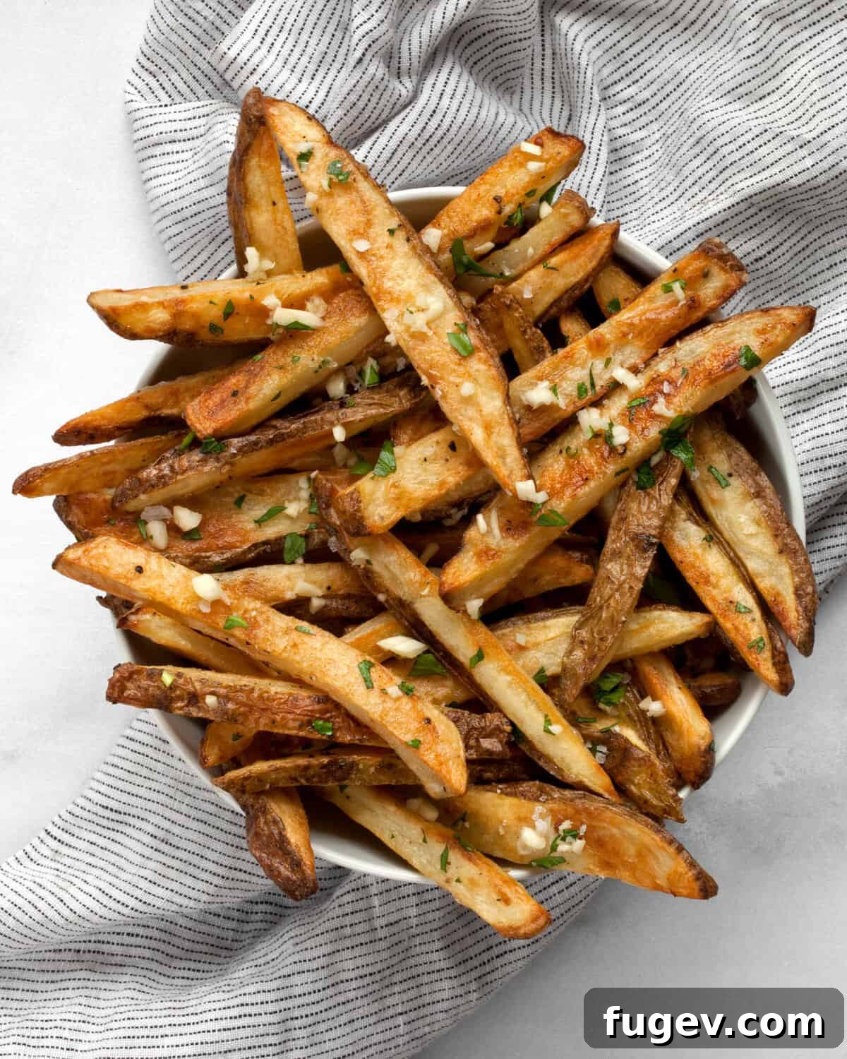 Quick & Crispy Garlic Oven Fries 2 A bowl filled with golden-brown, crispy oven baked garlic fries, garnished with fresh parsley.