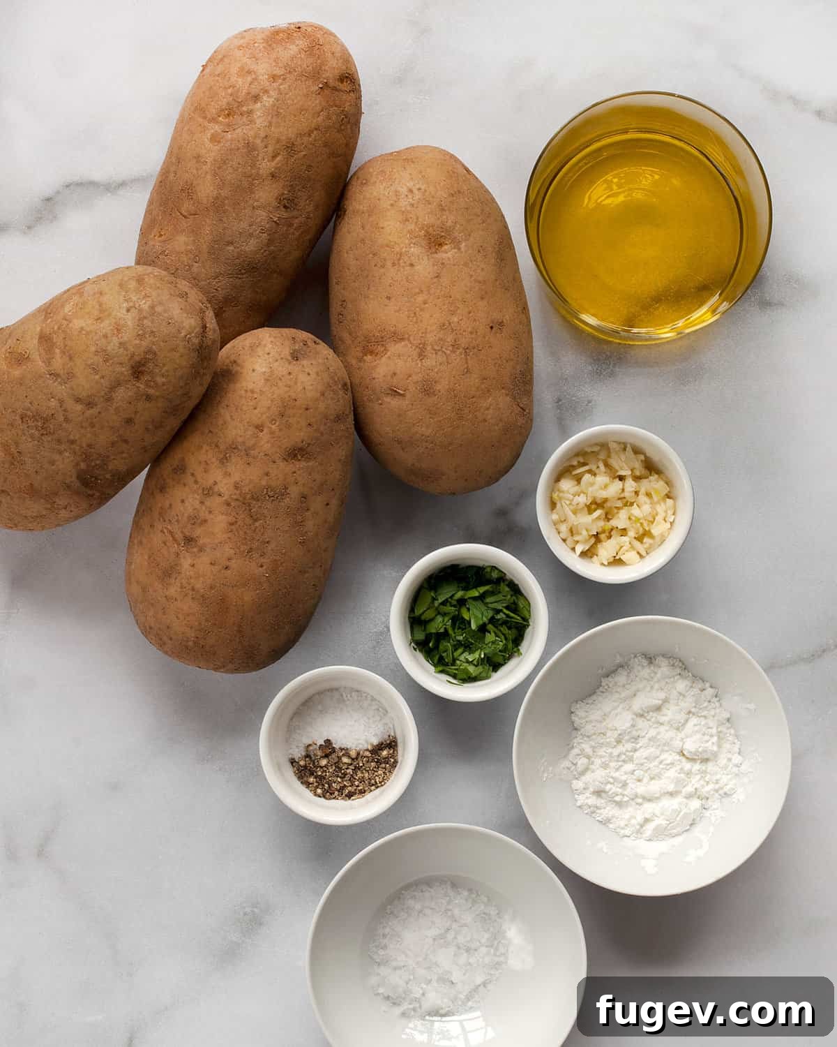 Quick & Crispy Garlic Oven Fries 3 Assortment of ingredients for baked garlic fries including whole Russet potatoes, olive oil, cornstarch, salt, pepper, fresh garlic cloves, and parsley.
