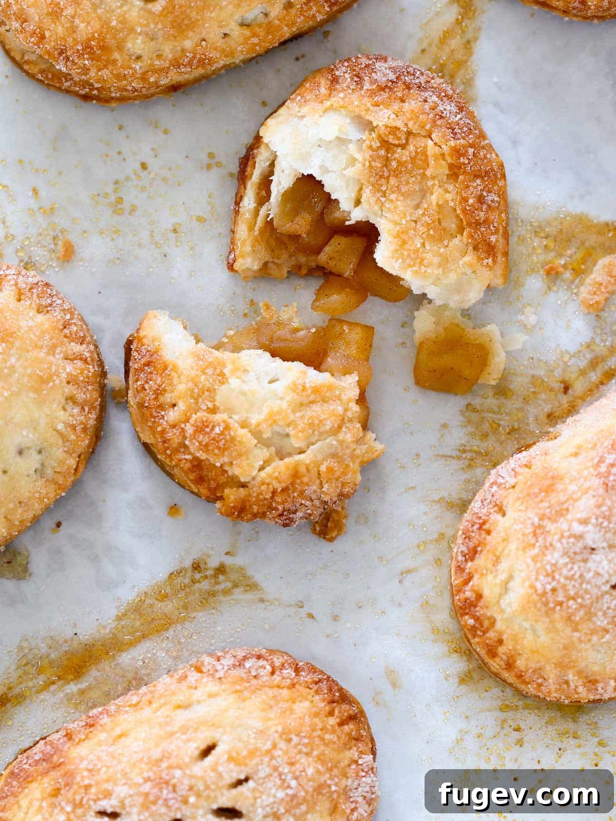 Flaky Apple Turnovers 2 Golden brown apple hand pies baked to perfection on a baking sheet, showcasing their flaky crust and sugary topping.