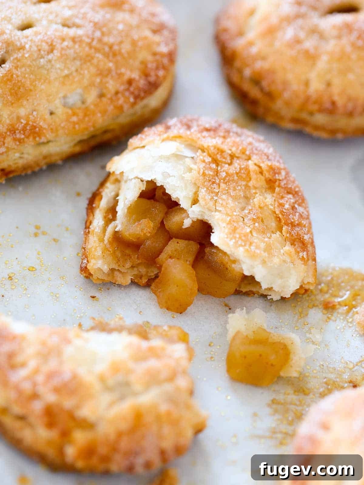 Flaky Apple Turnovers 13 An overhead view of a broken apple hand pie on a baking sheet, with the warm apple filling visibly spilling out slightly, showcasing its texture.