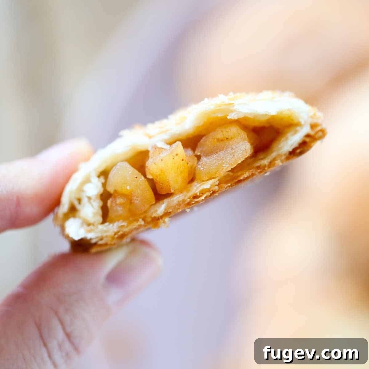 Flaky Apple Turnovers 3 A person holding a half-eaten apple hand pie, showing the delicious apple filling inside.