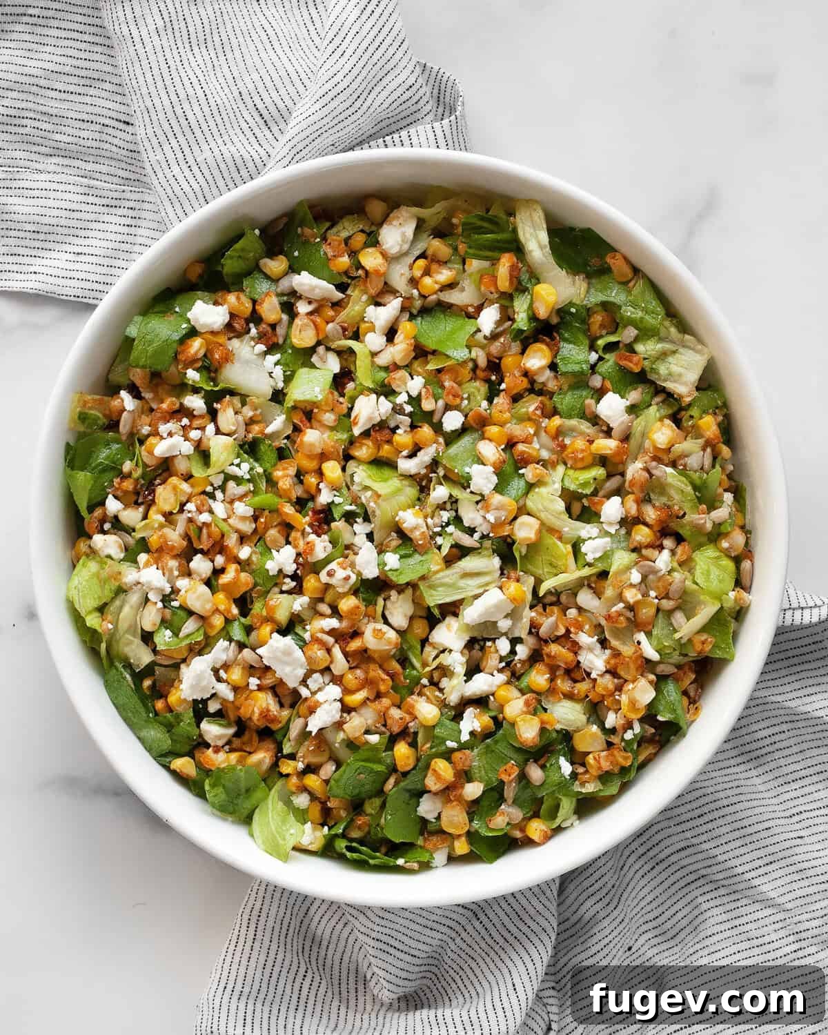 Smoky Roasted Corn Salad 2 A vibrant bowl of roasted corn salad, featuring golden corn kernels, crisp romaine, crumbled feta, and green scallions, glistening with vinaigrette.