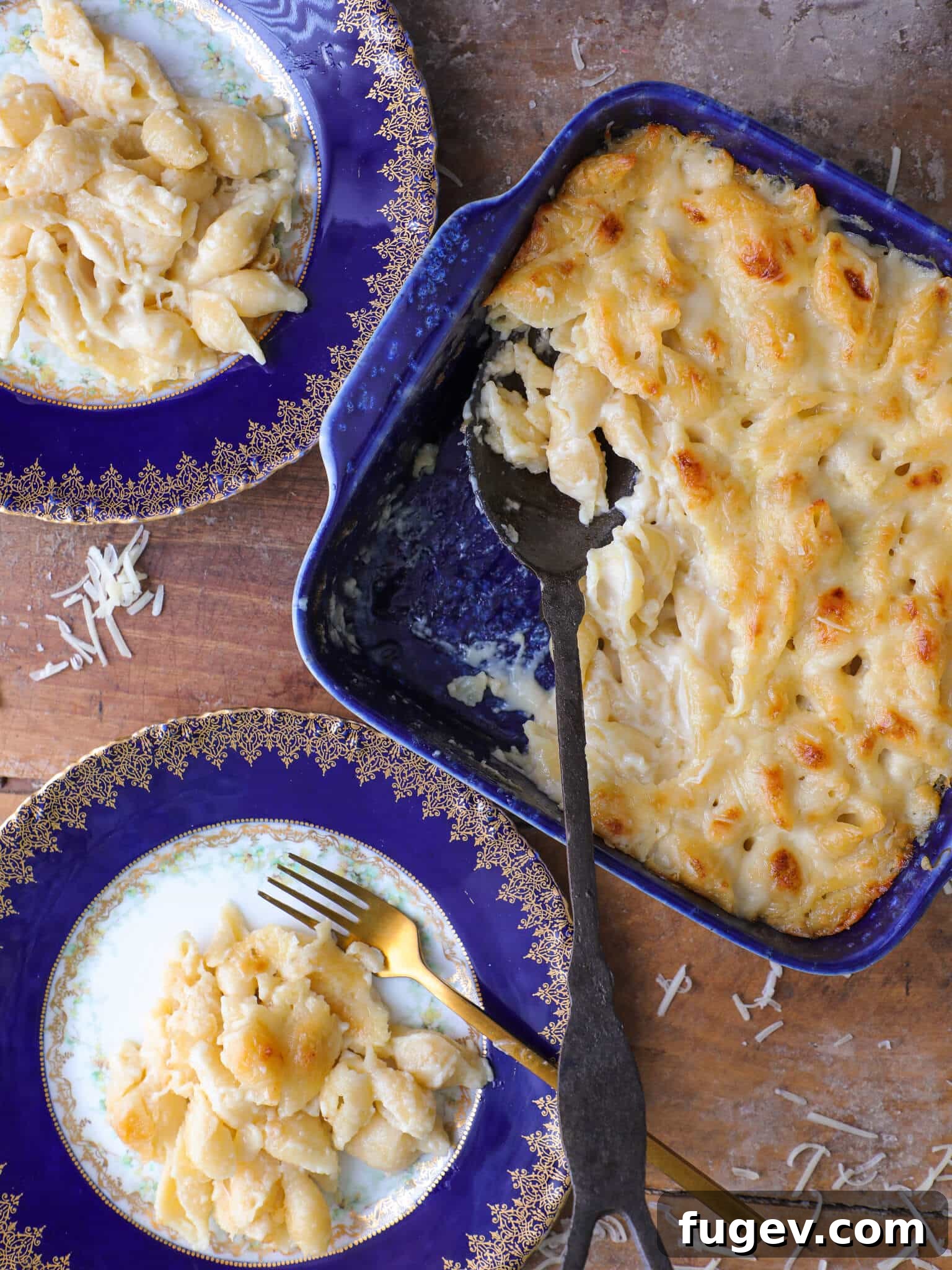 Velvety White Cheddar Mac 2 Two plates of white cheddar mac and cheese next to a blue baking dish full of the rest.