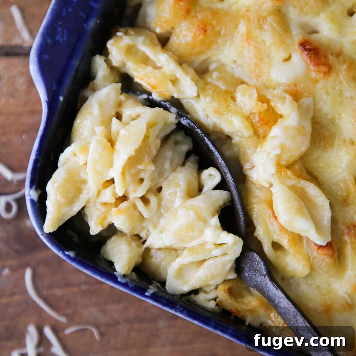 Velvety White Cheddar Mac 3 A spoon serving a portion of white cheddar mac and cheese from a blue baking dish.