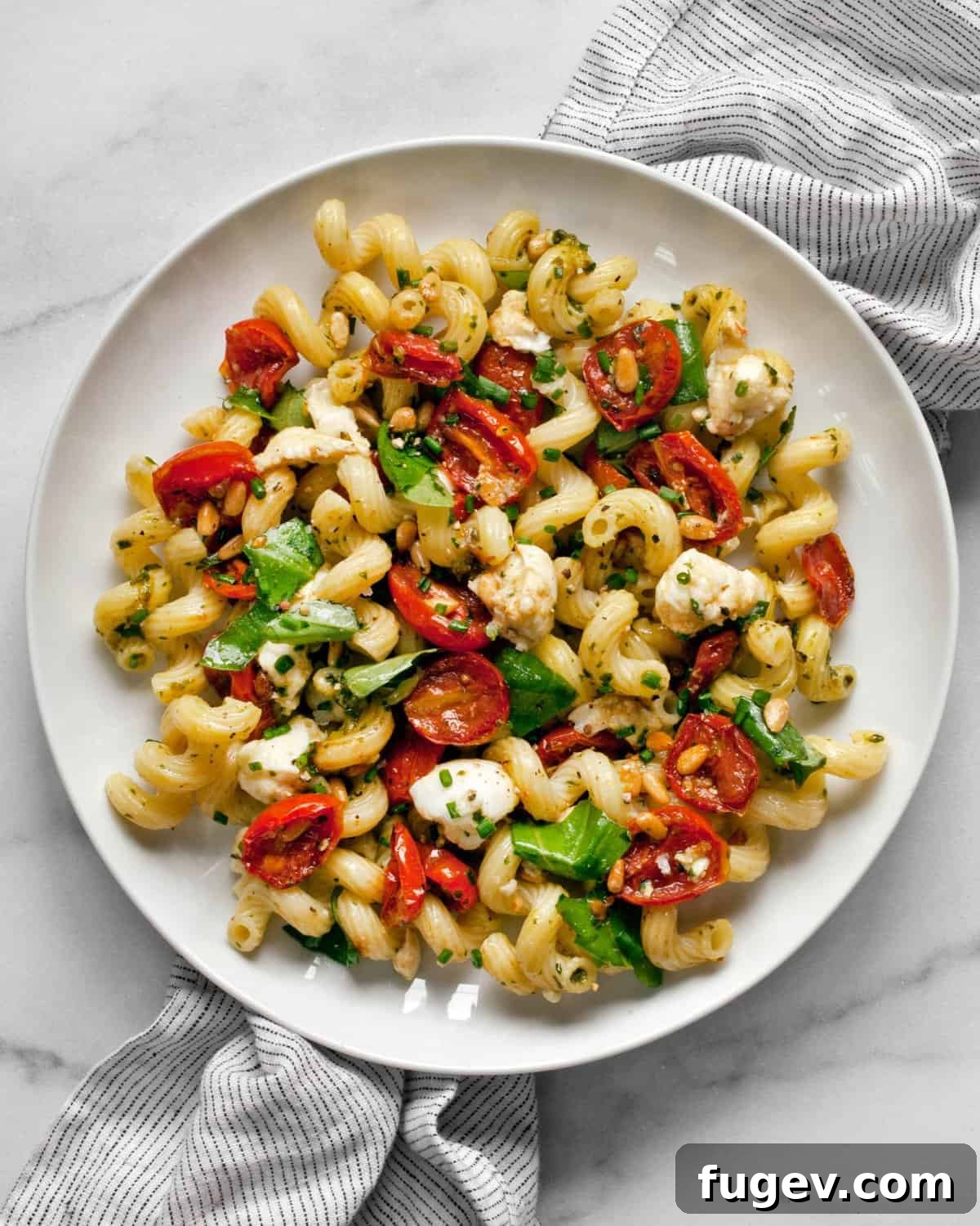 Sun-Kissed Tomato Pesto Pasta Salad 3 Pesto pasta salad with roasted tomatoes and mozzarella on a plate, garnished with fresh basil.