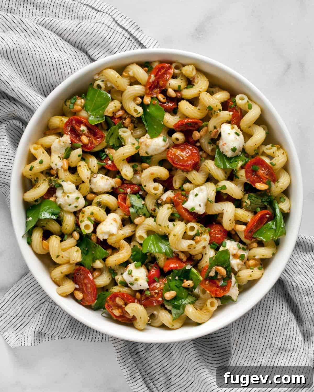 Sun-Kissed Tomato Pesto Pasta Salad 9 A large bowl of roasted tomato pesto pasta salad with mozzarella, garnished with fresh basil leaves.