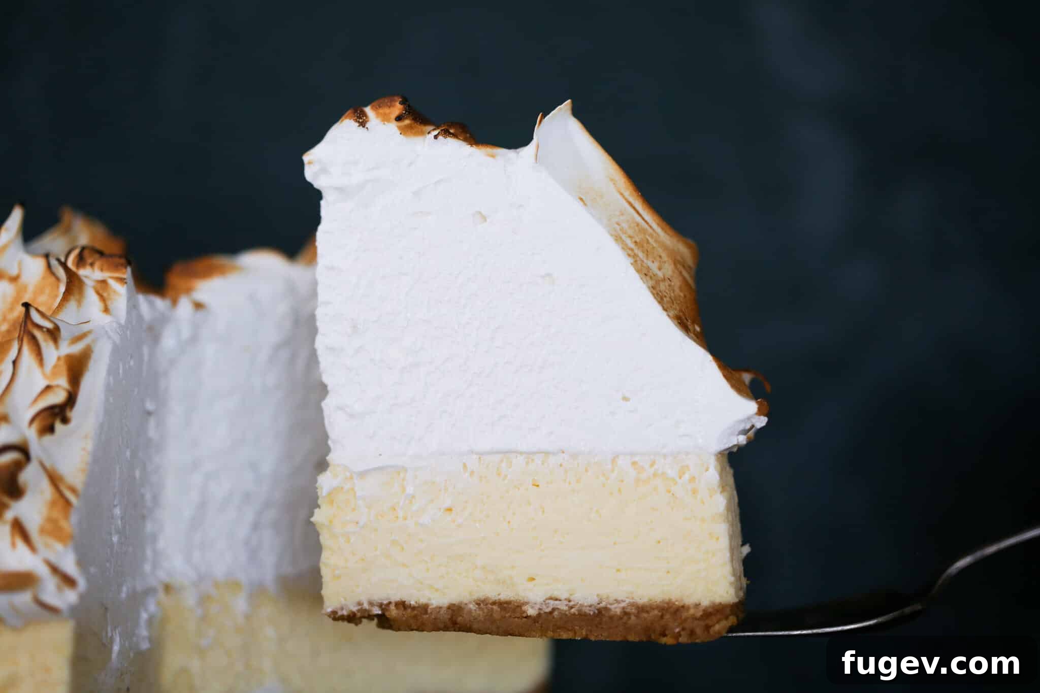 Zesty Lemon Cloud Cheesecake 4 A beautiful slice of Lemon Meringue Cheesecake on a silver cake server, ready to be enjoyed.