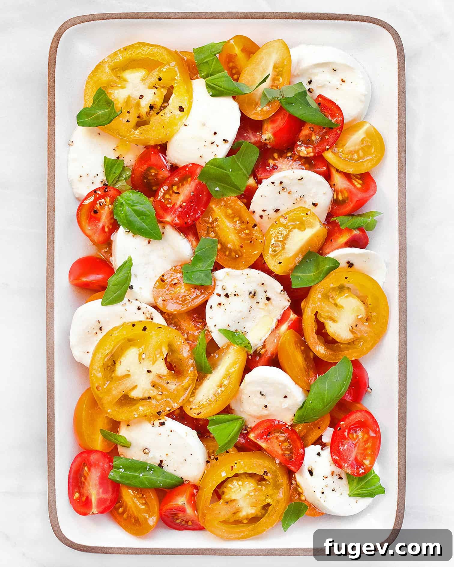 Fresh Italian Trio 2 Fresh Caprese salad beautifully arranged on a white platter, featuring vibrant red tomatoes, white mozzarella, and green basil, drizzled with olive oil.