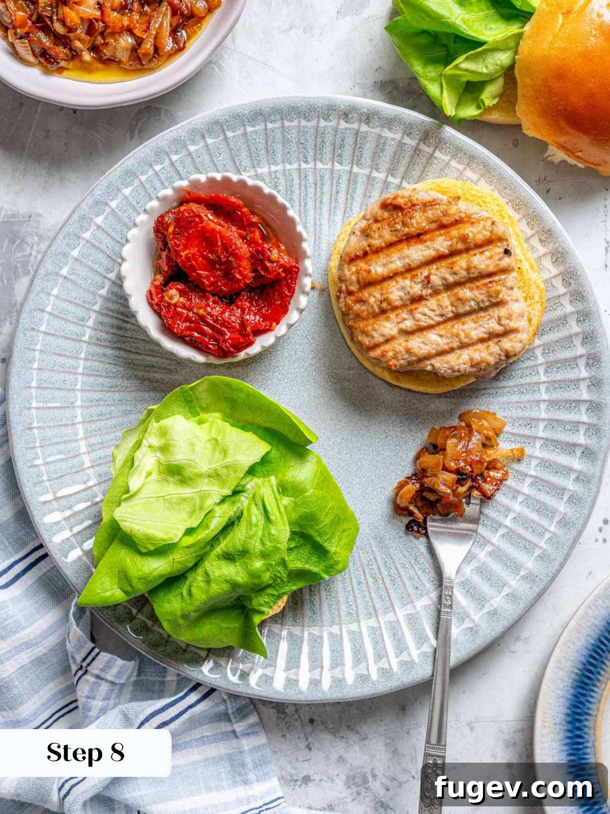 Juicy Homemade Turkey Burgers 11 Cooked turkey burger patties resting on a plate with fresh lettuce, sun-dried tomatoes, and caramelized onions, ready for assembly.