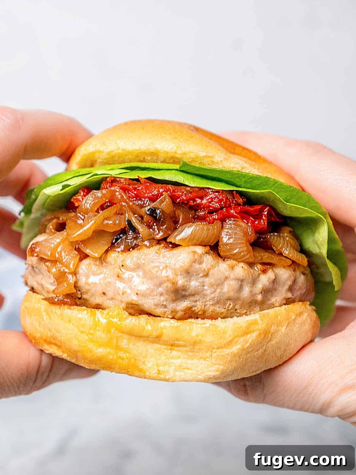 Juicy Homemade Turkey Burgers 12 A hand holding a gourmet turkey burger, revealing juicy patty, caramelized onions, fresh lettuce, and a soft brioche bun.