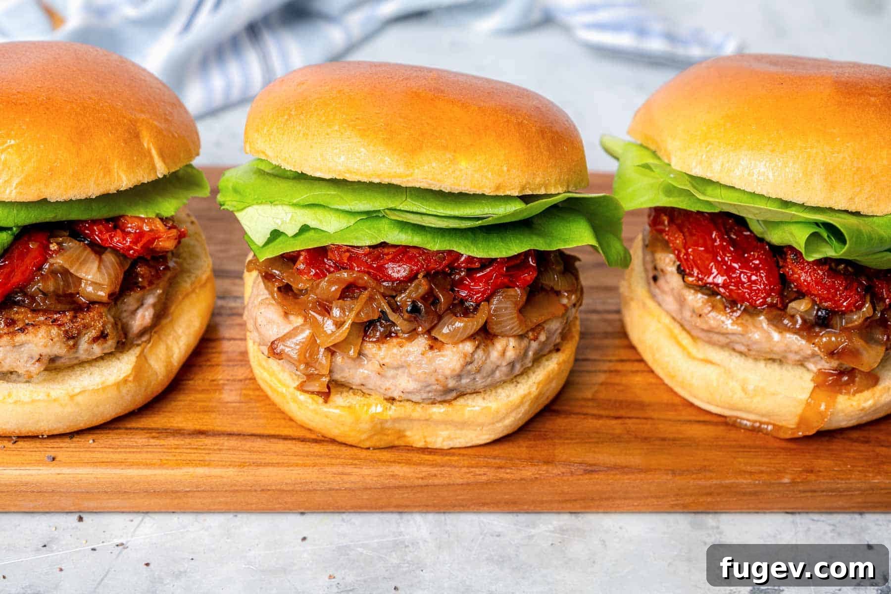 Juicy Homemade Turkey Burgers 4 Three perfectly assembled turkey burgers, topped with caramelized onions and lettuce, presented on a rustic wooden board.