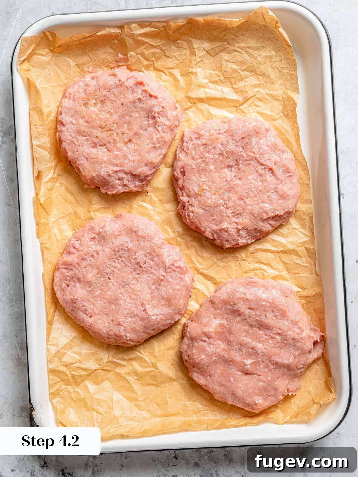 Juicy Homemade Turkey Burgers 9 Four perfectly formed, thin turkey burger patties with dimples, resting on parchment paper.