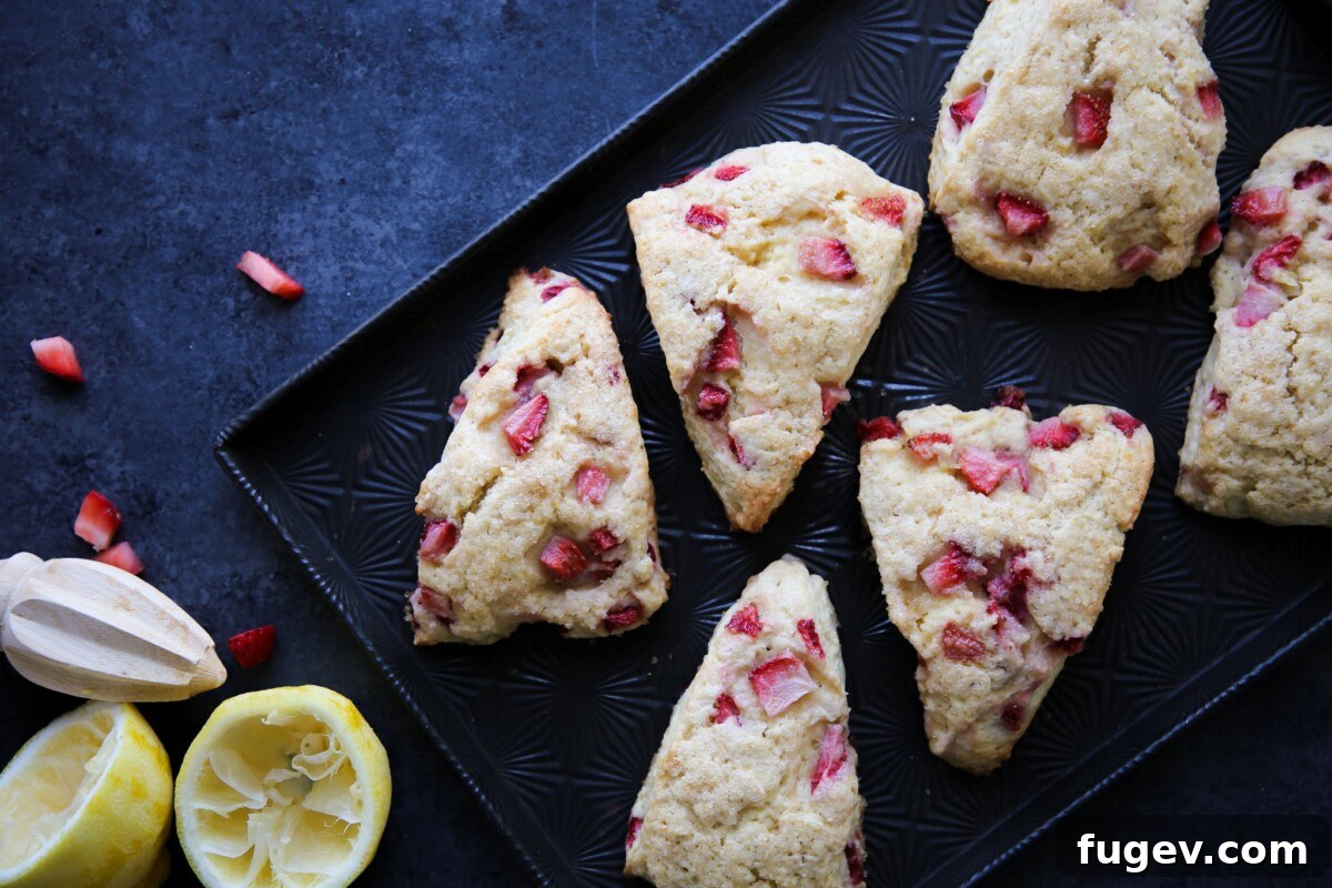 Sweet Summer Strawberry Scones 3 Strawberry Lemon Scones arranged on a black baking sheet with fresh lemons beside them.