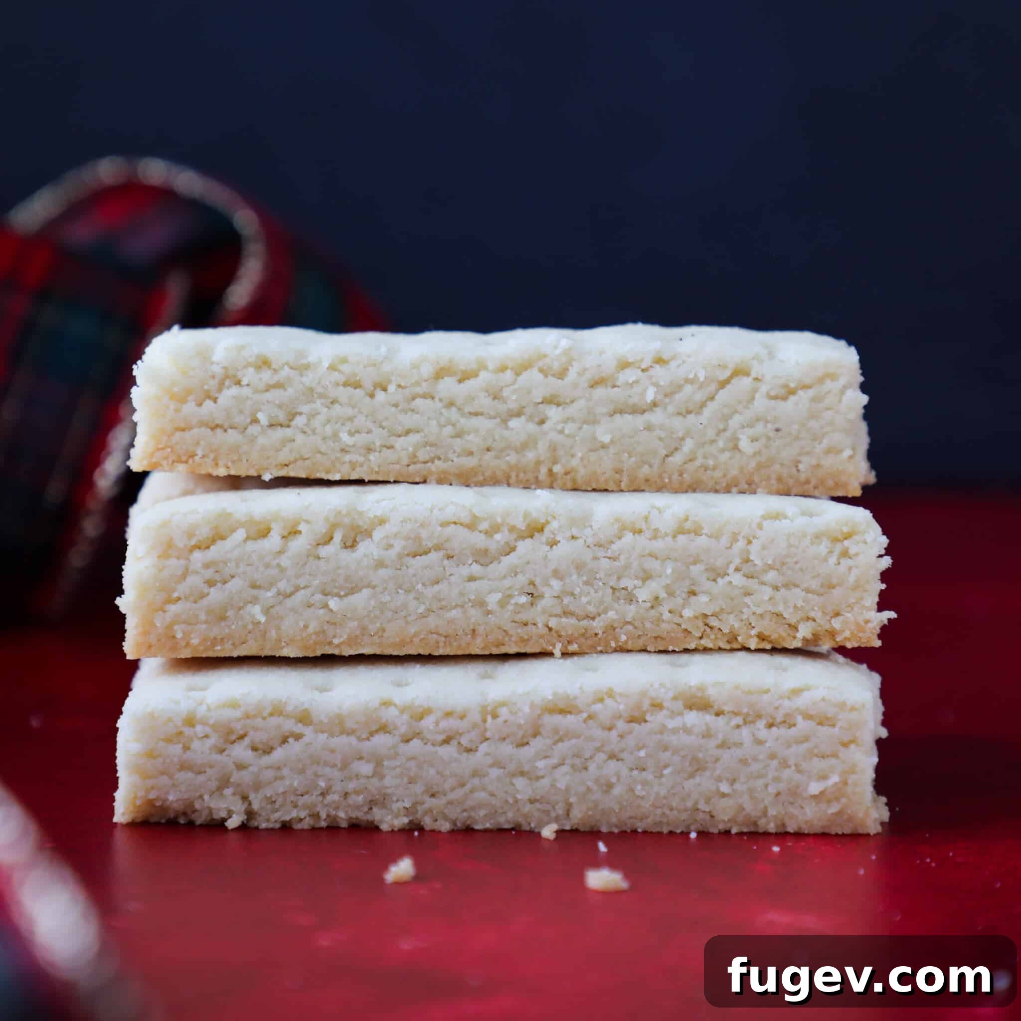 Buttery Scottish Shortbread 4 A perfectly arranged stack of three Scottish shortbread fingers rests on a vibrant red countertop, showcasing their golden hue and inviting texture.