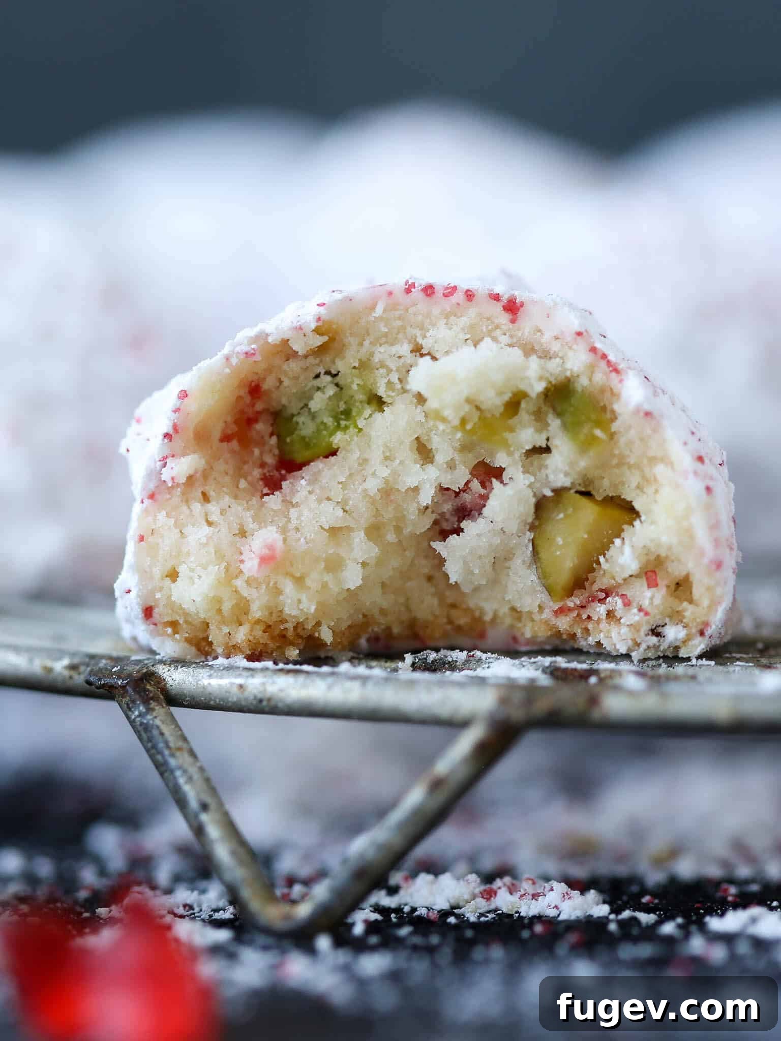 Ruby Red Pistachio Snow Kisses 2 Crumbly Cherry Pistachio Snowball Cookie revealing its tender interior and colorful additions