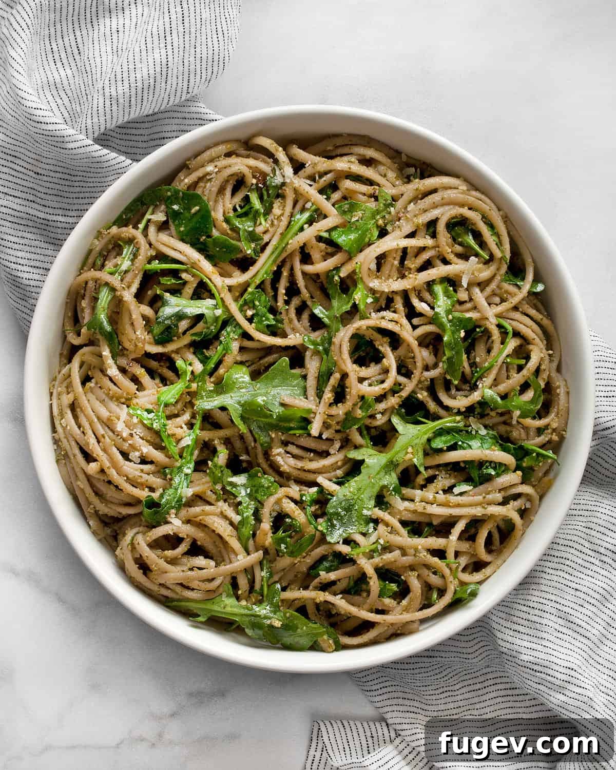 Peppery Arugula Pesto Pasta 2 A large bowl filled with vibrant green arugula pasta, garnished with fresh arugula leaves and grated Parmesan cheese.