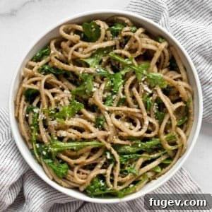 A small bowl of vibrant green arugula pesto pasta, garnished with fresh herbs.