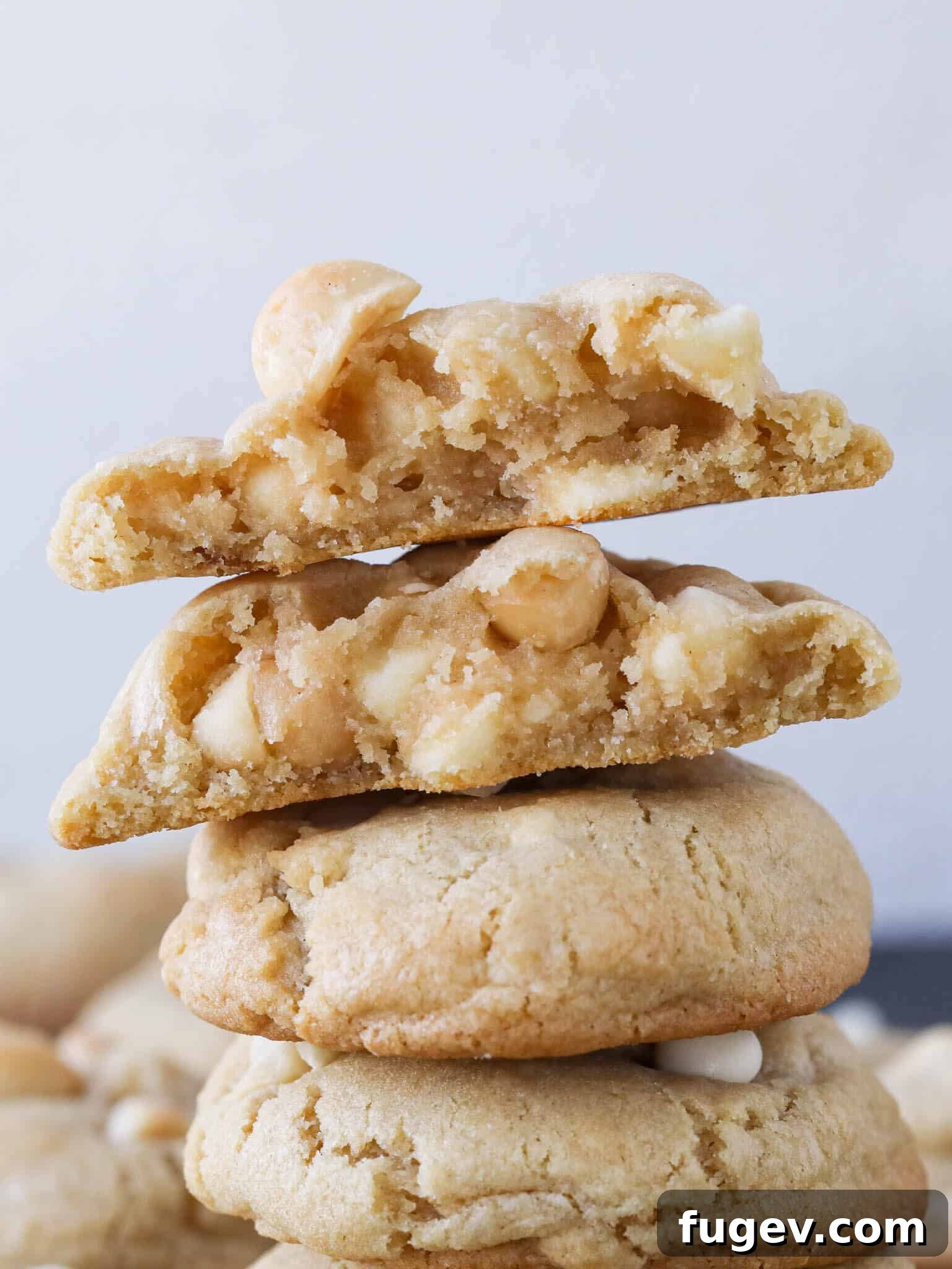 Creamy White Chocolate Macadamia Nut Delights 2 Stacked white chocolate macadamia nut cookies, with the top two broken in half to showcase the chewy interior and abundant mix-ins.