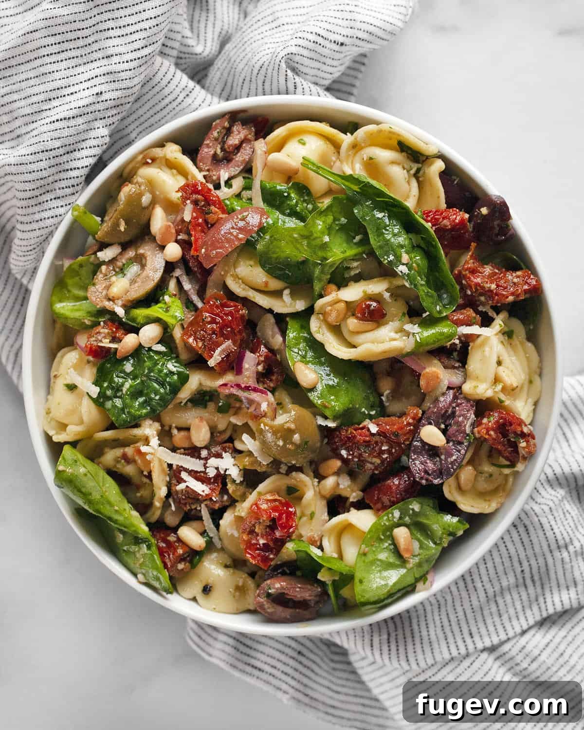 Vibrant Tortellini Salad 2 A small bowl of tortellini pasta salad featuring sun-dried tomatoes, olives, and spinach, perfectly dressed.