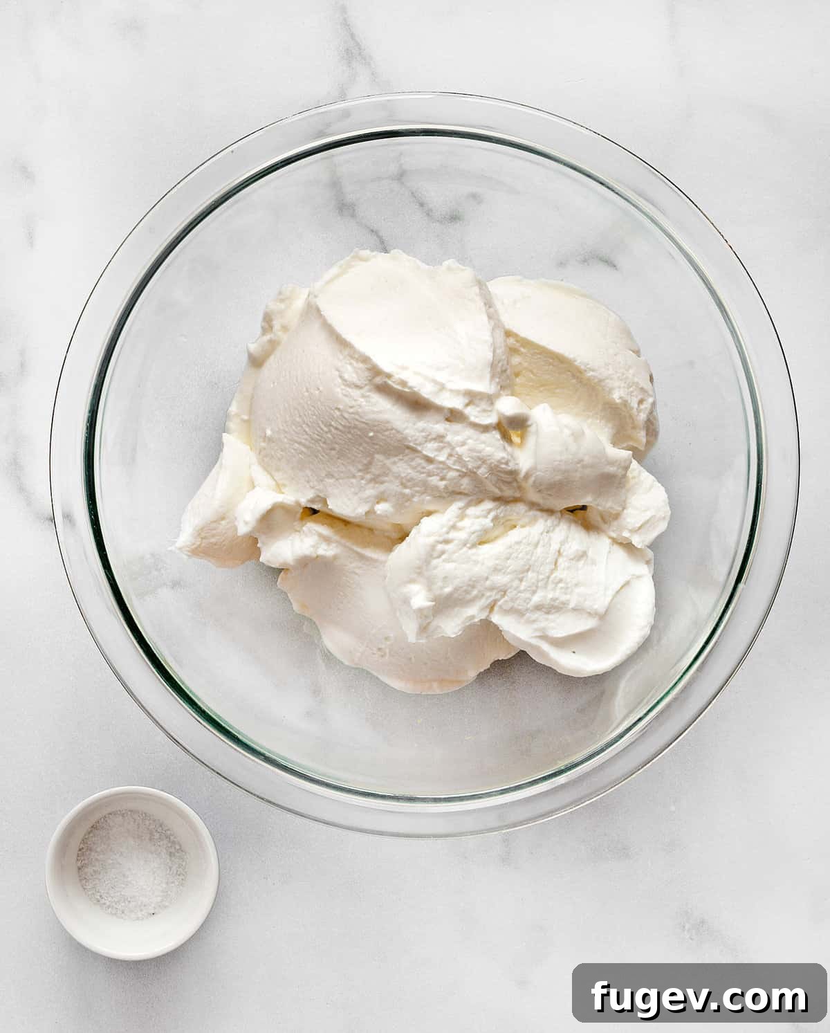 Homemade Labneh: The Greek Yogurt Secret 3 A large bowl filled with creamy Greek yogurt sits next to a small container of kosher salt, highlighting the simplicity of labneh's two core ingredients.