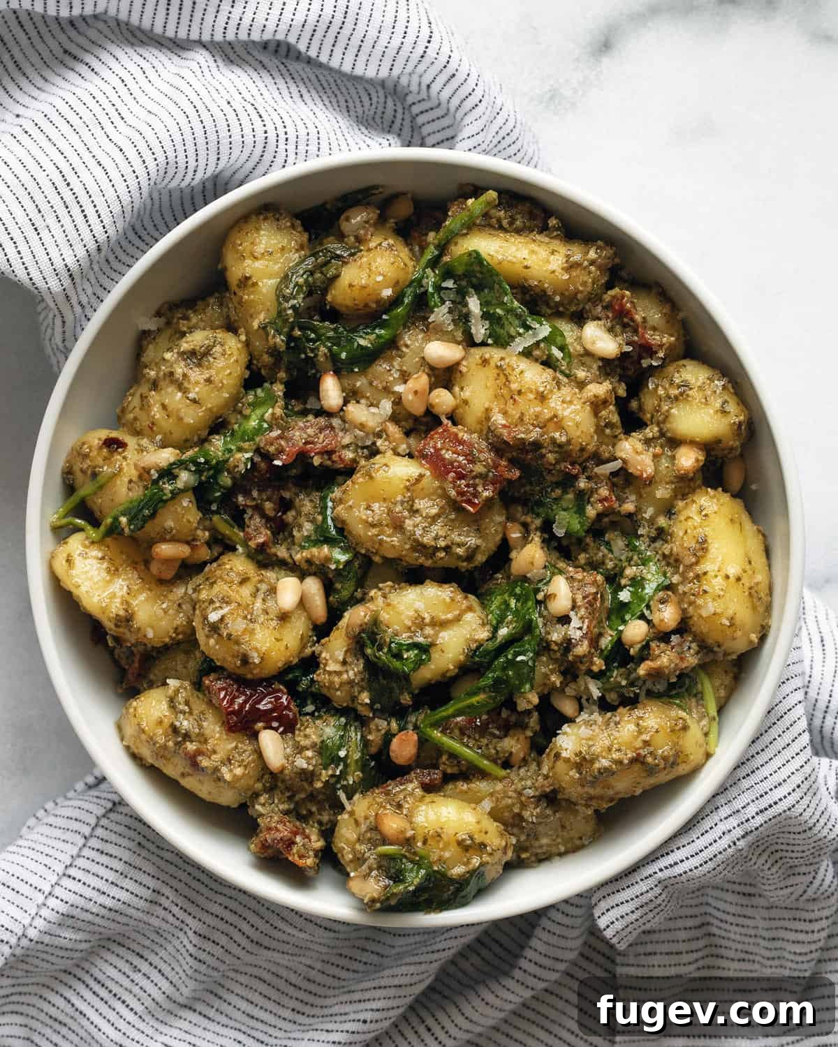 Tuscan Gnocchi with Sun-Dried Tomato Pesto 2 A small bowl of vibrant pesto gnocchi featuring sun-dried tomatoes, fresh spinach, and garnished with pine nuts and Parmesan.