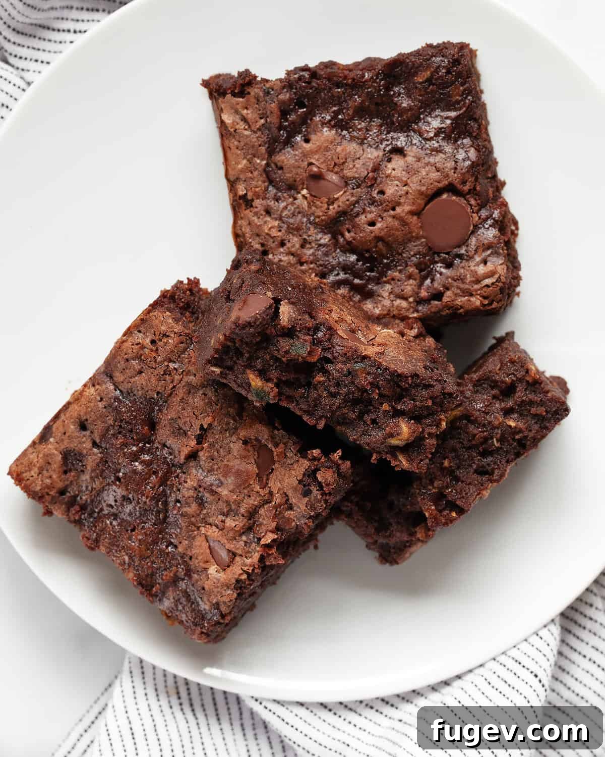 Sneaky Zucchini Brownie Bliss 8 Three perfectly baked zucchini brownies arranged on a white plate, one of which is broken in half to reveal its moist, fudgy interior.