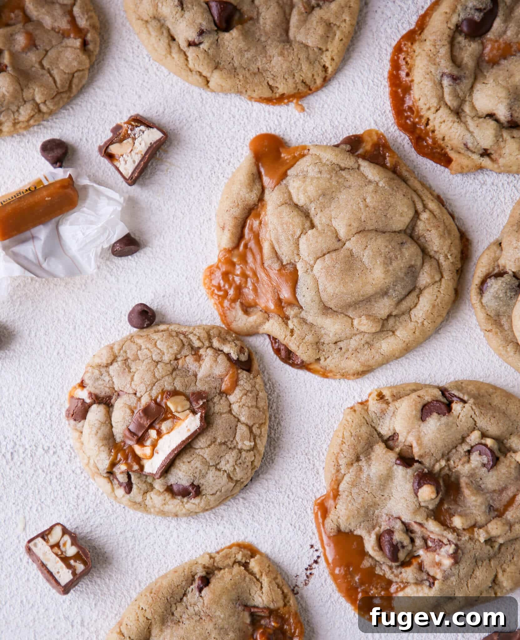 Molten Caramel Snickers Brown Butter Chocolate Chip Cookies 2 Caramel Stuffed Brown Butter Snickers Chocolate Chip Cookies arranged on white surface
