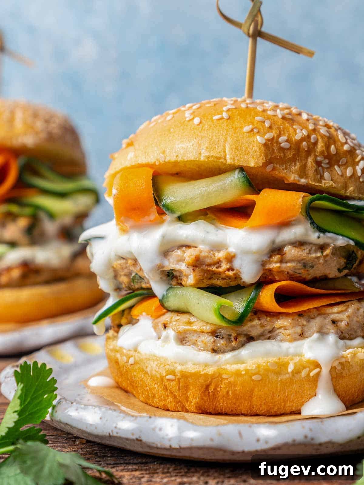 Succulent Chicken Burgers 2 Juicy chicken burger stacked high with crisp veggies and a creamy sauce on a brioche bun.