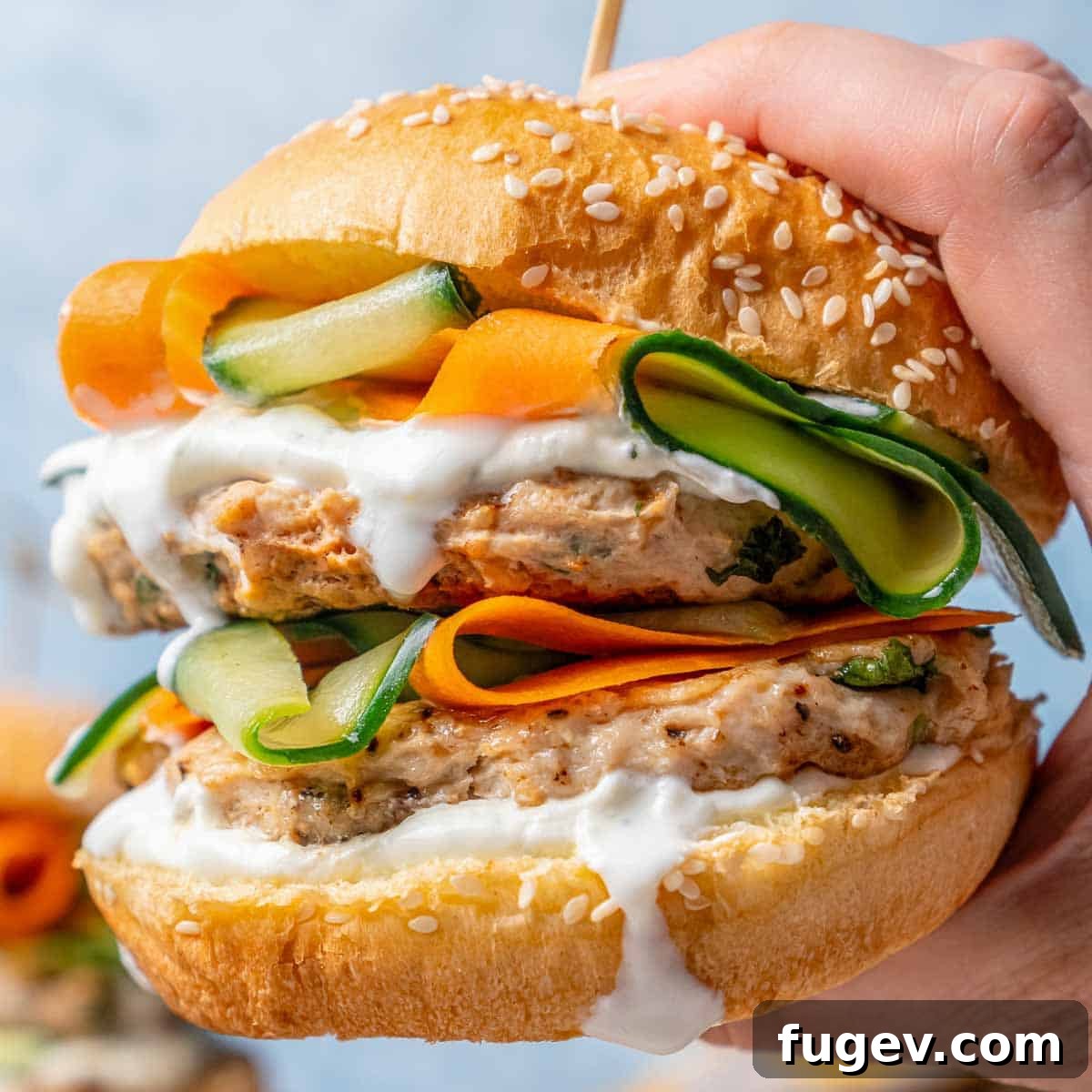 Succulent Chicken Burgers 3 Hand holding a perfectly grilled chicken burger with crisp lettuce and a generous dollop of white sauce.