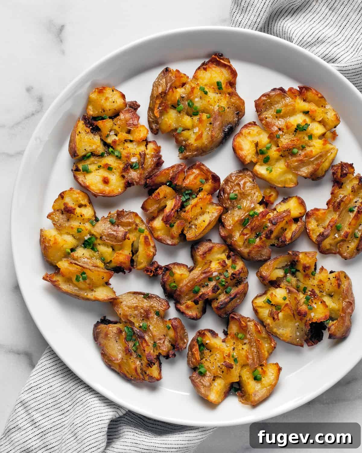 Crispy Smashed Potatoes 2 Roasted smashed potatoes on a plate, garnished with fresh herbs.