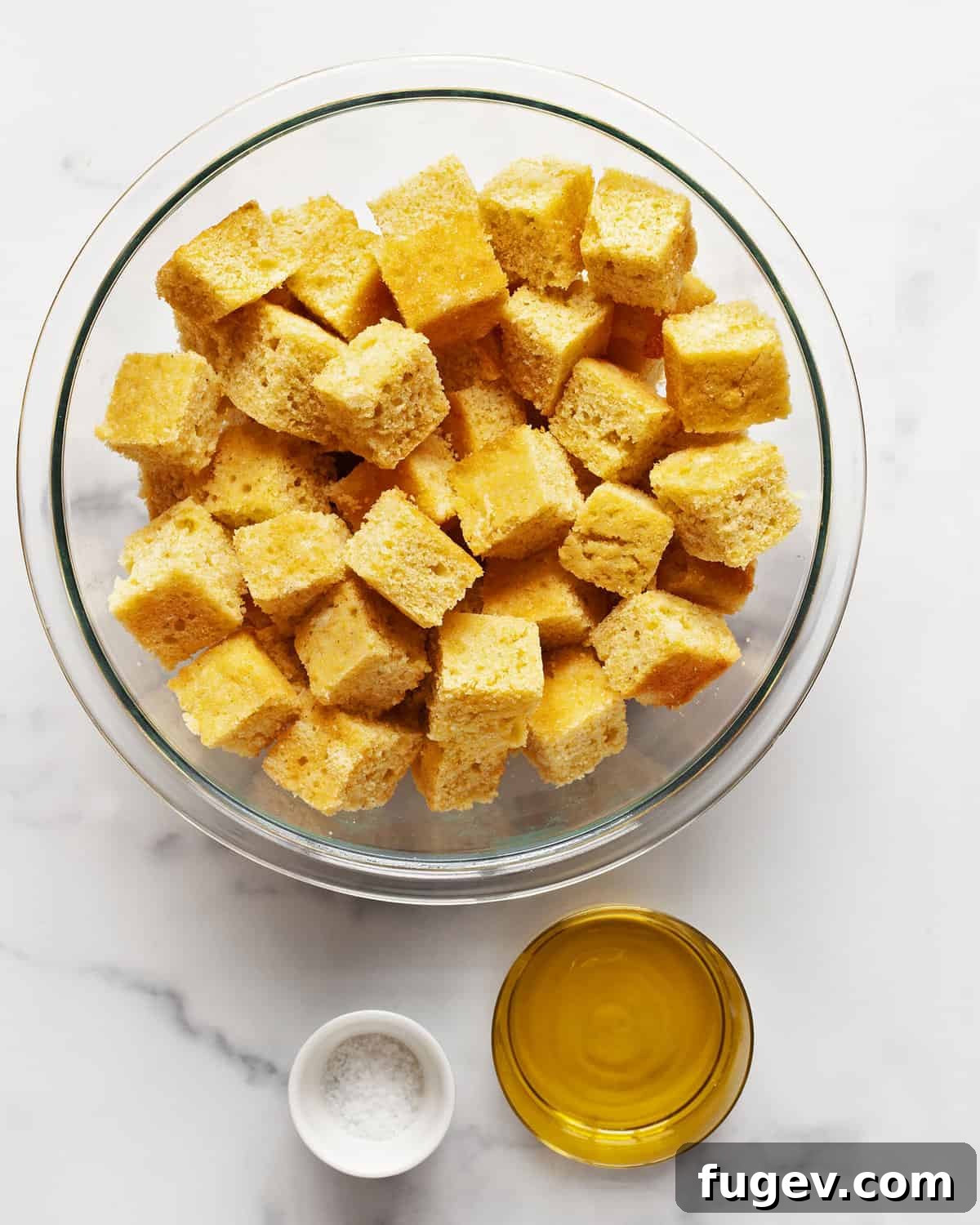 Golden Cornbread Bites 3 Cubed cornbread, a bottle of olive oil, and a pinch of salt on a wooden surface.