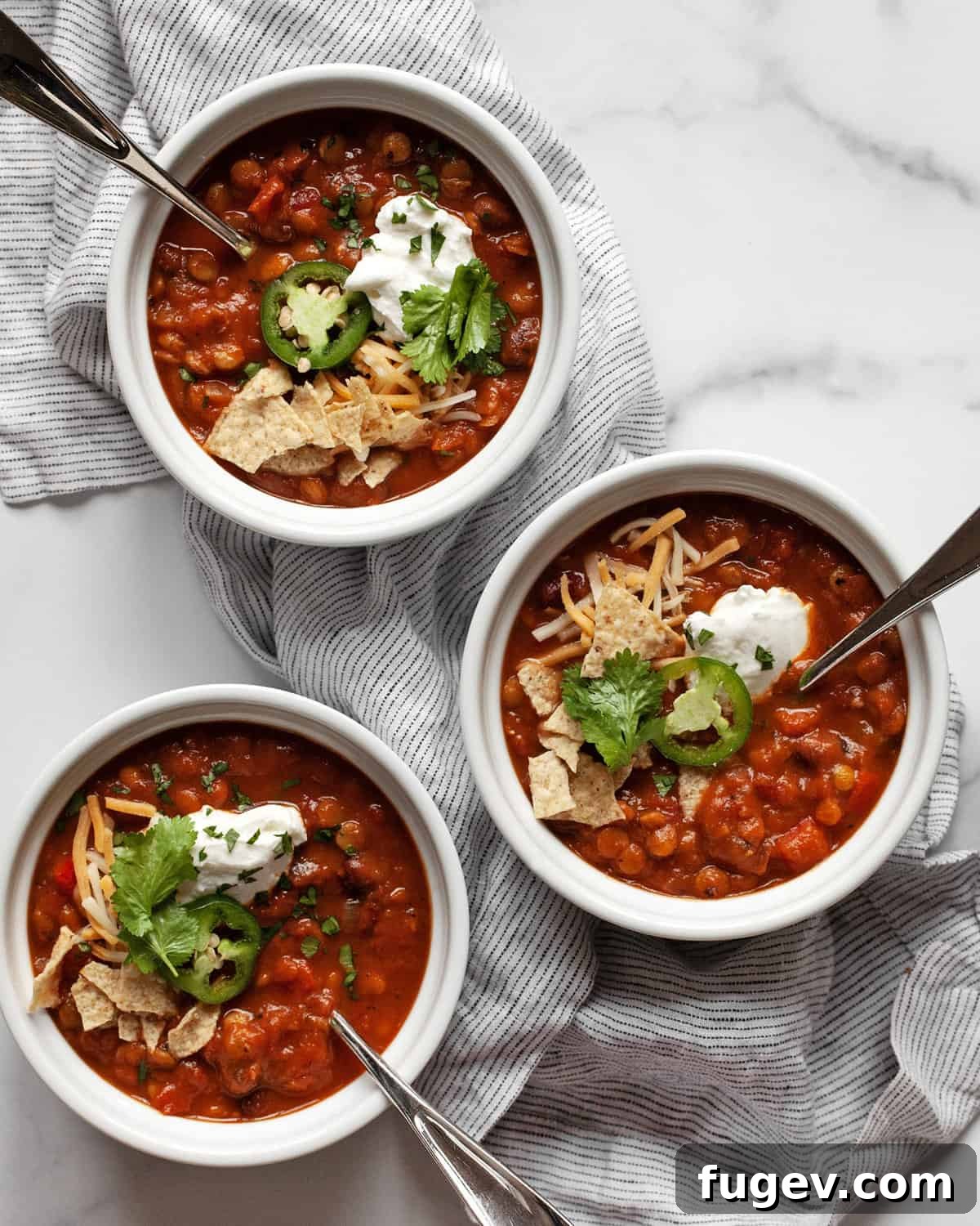 Hearty Pumpkin Lentil and Bean Chili 2 Three bowls of hearty vegan pumpkin chili garnished with fresh cilantro and avocado slices, perfect for a fall meal.