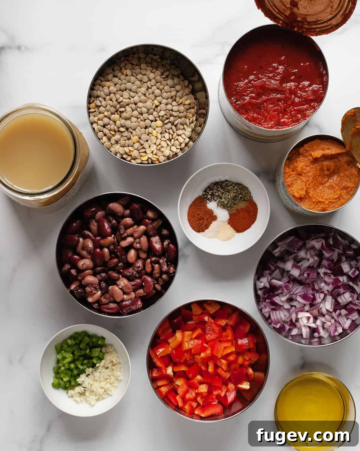 Hearty Pumpkin Lentil and Bean Chili 3 A vibrant display of fresh and canned ingredients for pumpkin chili, including pumpkin puree, various beans, lentils, tomatoes, bell peppers, garlic, jalapeños, vegetable broth, and a selection of dried spices.