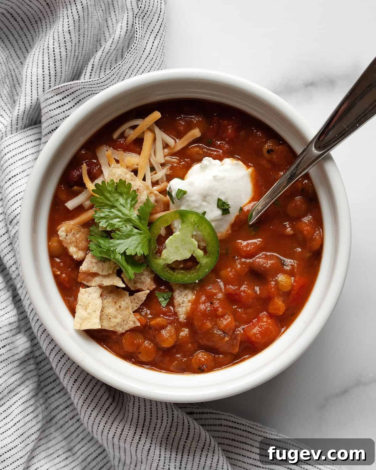 Hearty Pumpkin Lentil and Bean Chili 6 A beautifully presented bowl of vegan pumpkin chili, generously topped with fresh cilantro, creamy avocado slices, and a dollop of sour cream, ready to be enjoyed.
