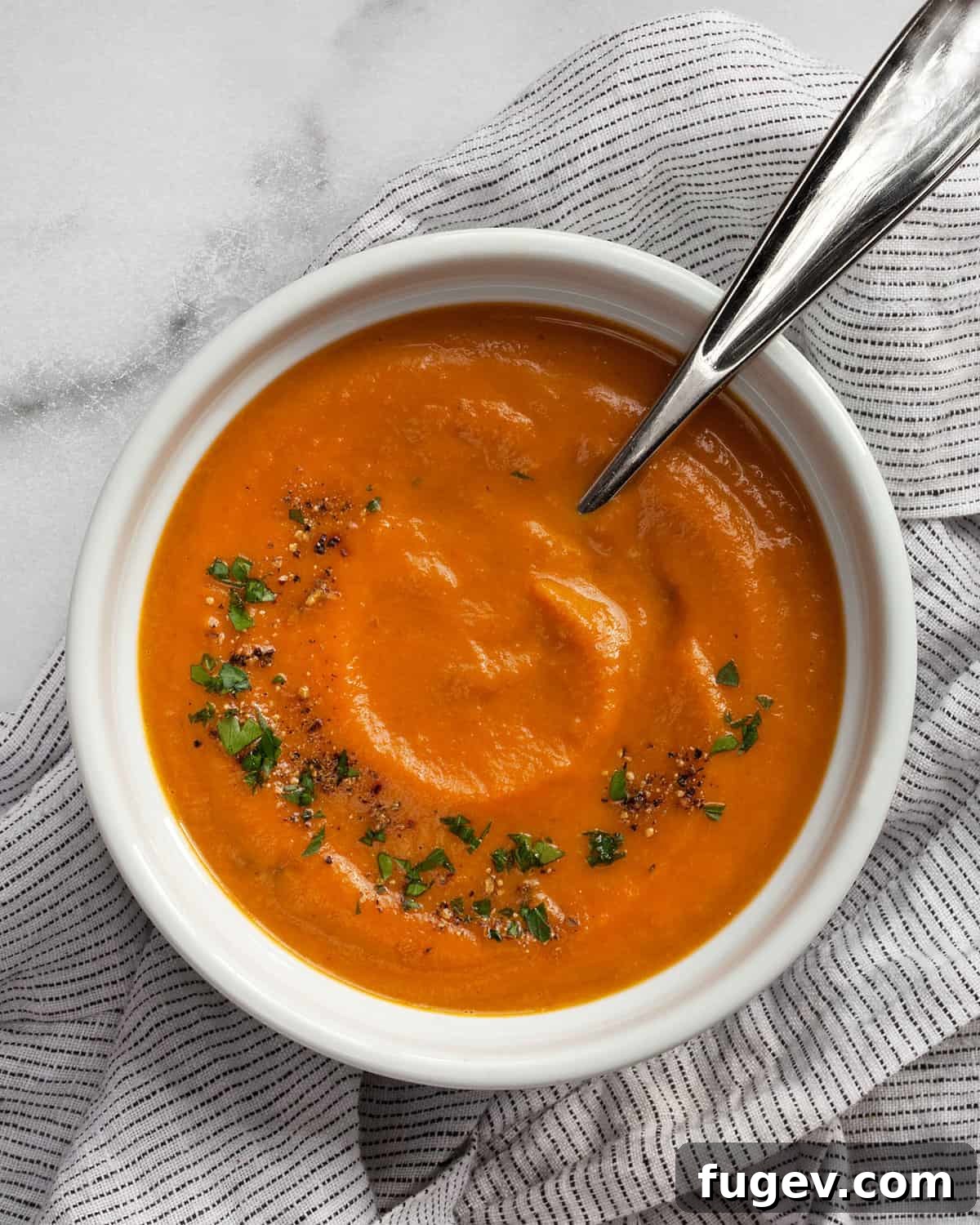 Velvety Roasted Carrot Bisque 2 A beautiful bowl of rich, orange roasted carrot soup, garnished with fresh chopped parsley and a sprinkle of black pepper, served on a rustic wooden surface.