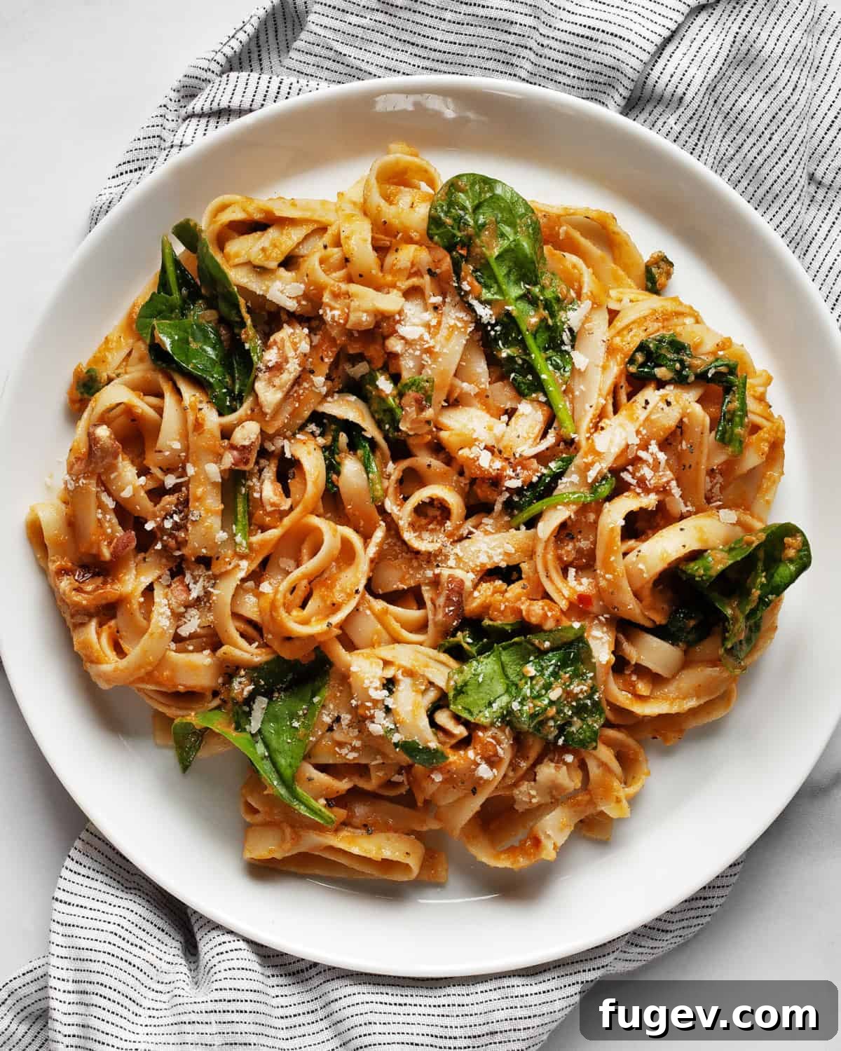 Creamy Pumpkin Spinach Pasta 2 A plate of creamy pumpkin pasta garnished with fresh spinach, walnuts, and grated Parmesan cheese, ready to be enjoyed.