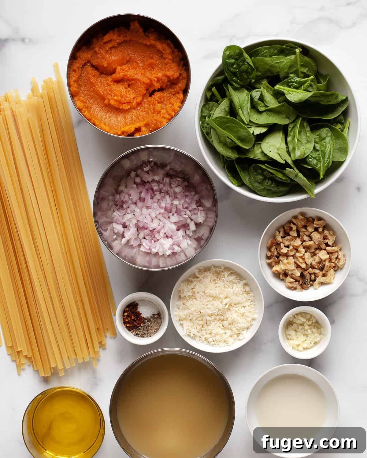 Creamy Pumpkin Spinach Pasta 3 Key ingredients for pumpkin pasta laid out: pumpkin puree, pasta, fresh spinach, walnuts, Parmesan cheese, milk, vegetable broth, shallots, aromatic spices, and garlic.