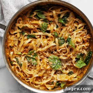 Creamy pumpkin pasta with spinach, walnuts, and Parmesan in a serving pan.