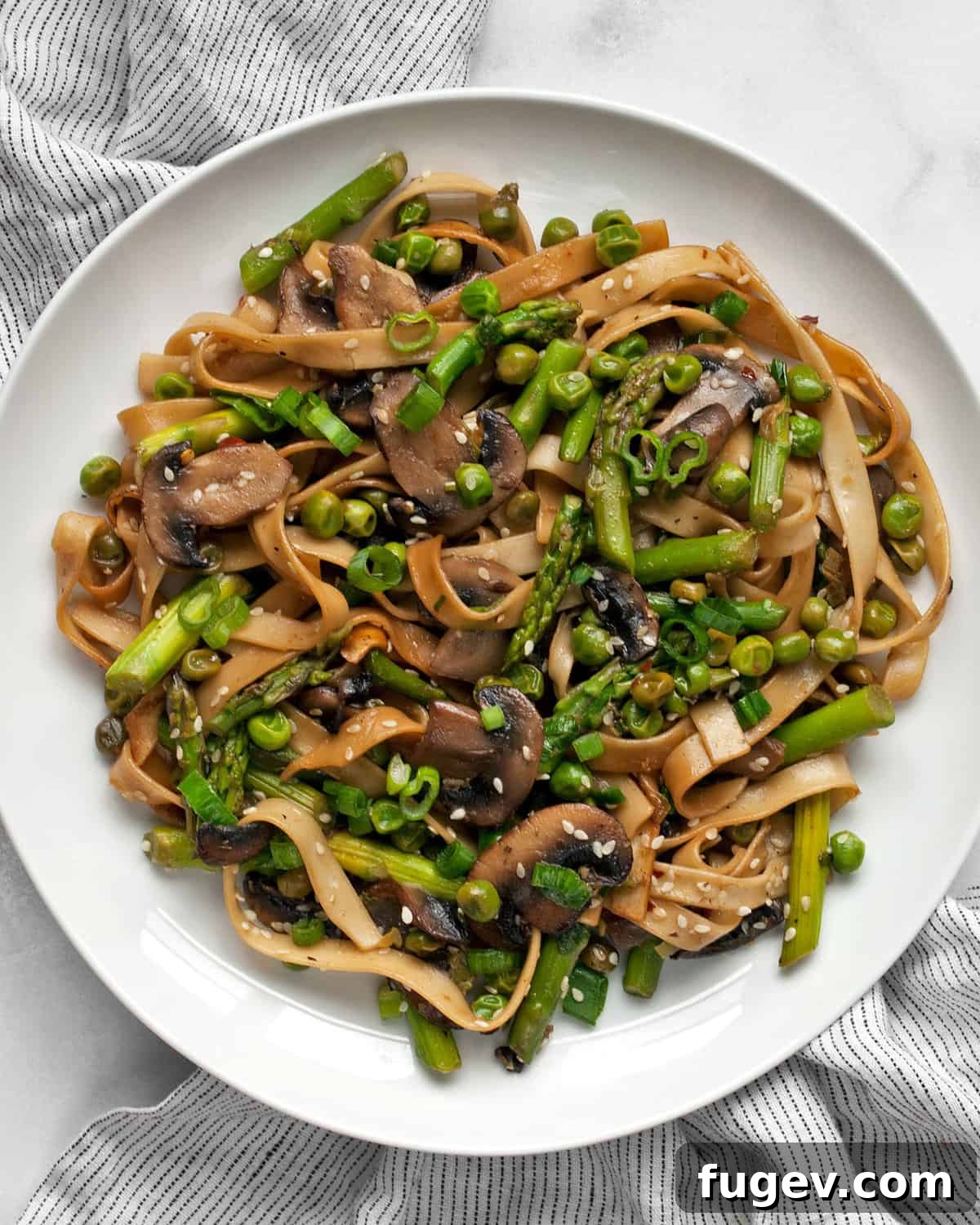 Vibrant Asparagus, Mushroom and Pea Stir-Fry 2 A beautifully plated asparagus stir-fry with udon noodles, mushrooms, and peas, garnished with sesame seeds and fresh scallions.