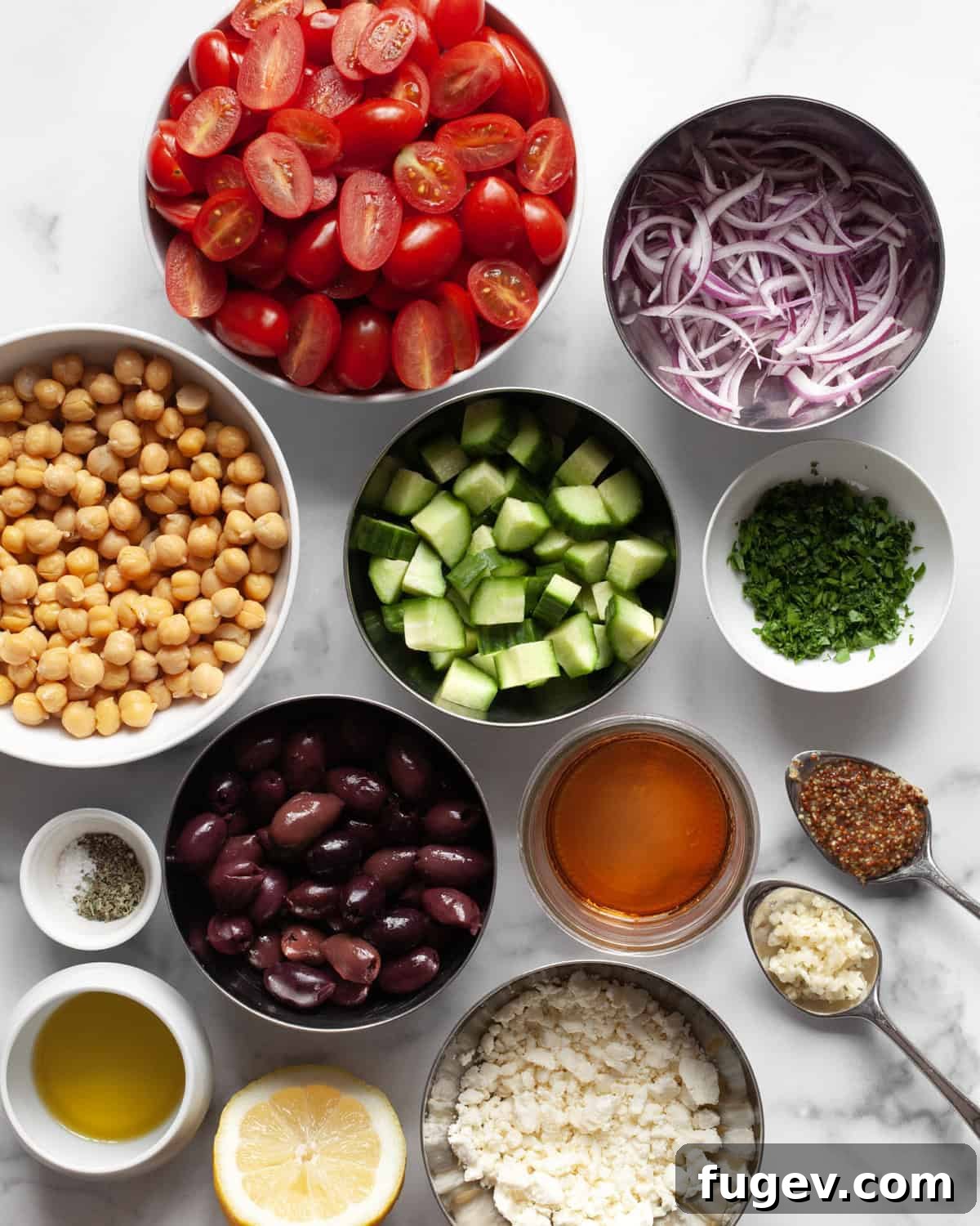 Mediterranean Chickpea Salad 3 Fresh ingredients for Greek chickpea salad including halved cherry tomatoes, cucumbers, Kalamata olives, red onions, crumbled feta, fresh parsley, and a small bowl of vinaigrette.