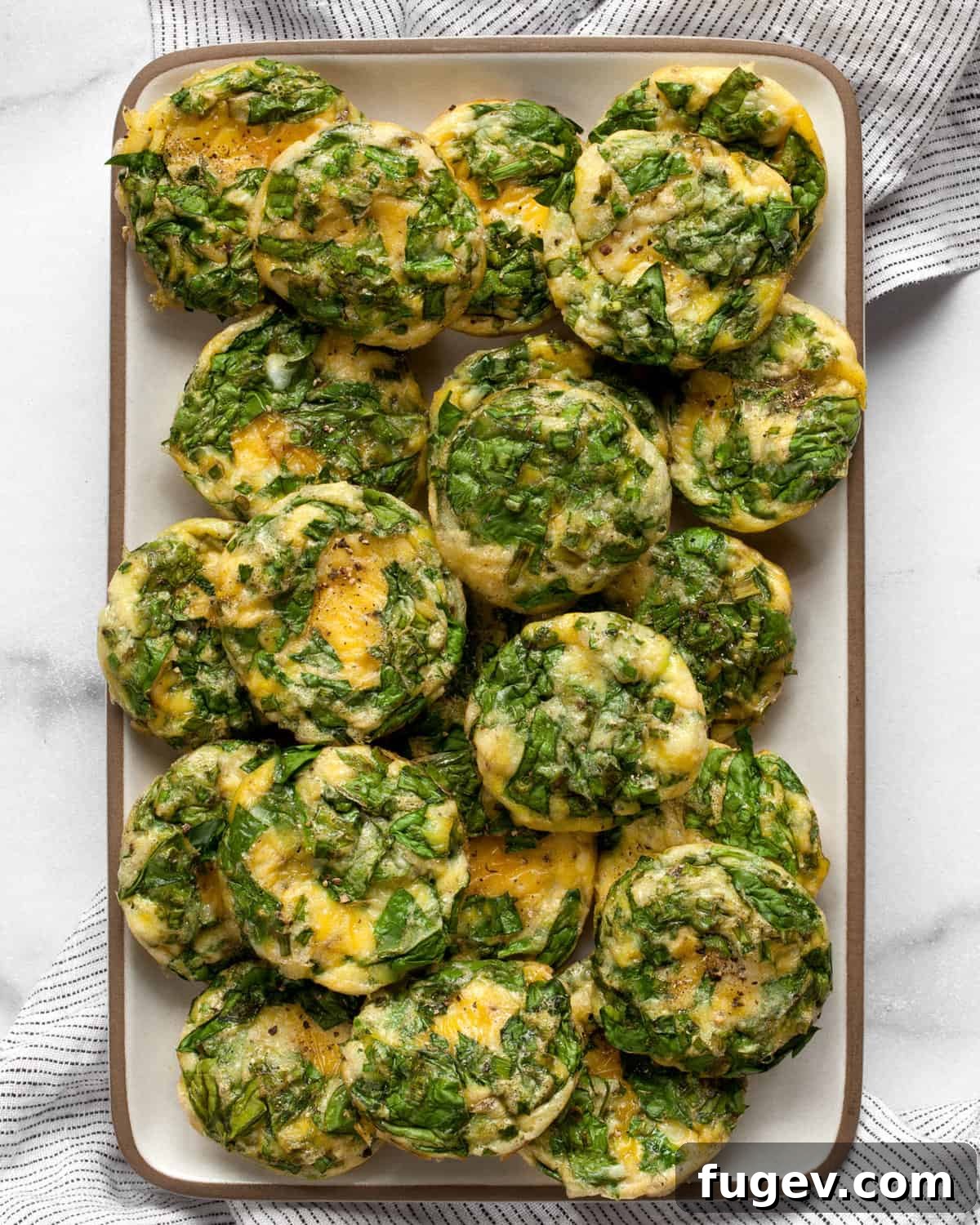 Savory Spinach & Parmesan Frittata Bites 2 A rectangular plate showcasing several golden-brown mini frittatas, garnished with fresh herbs.